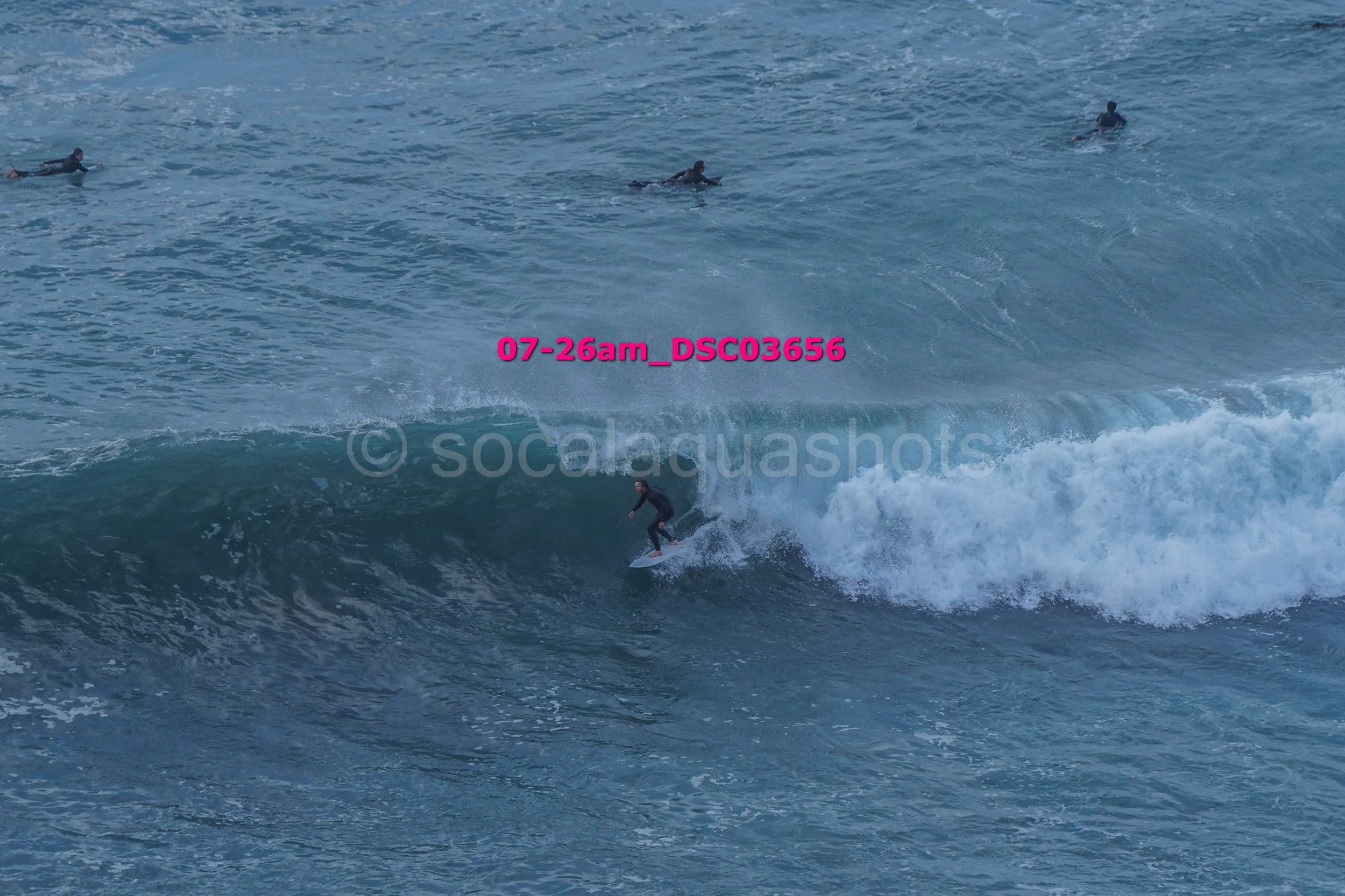 A person surfing on a wave in the ocean with several other surfers in the background.