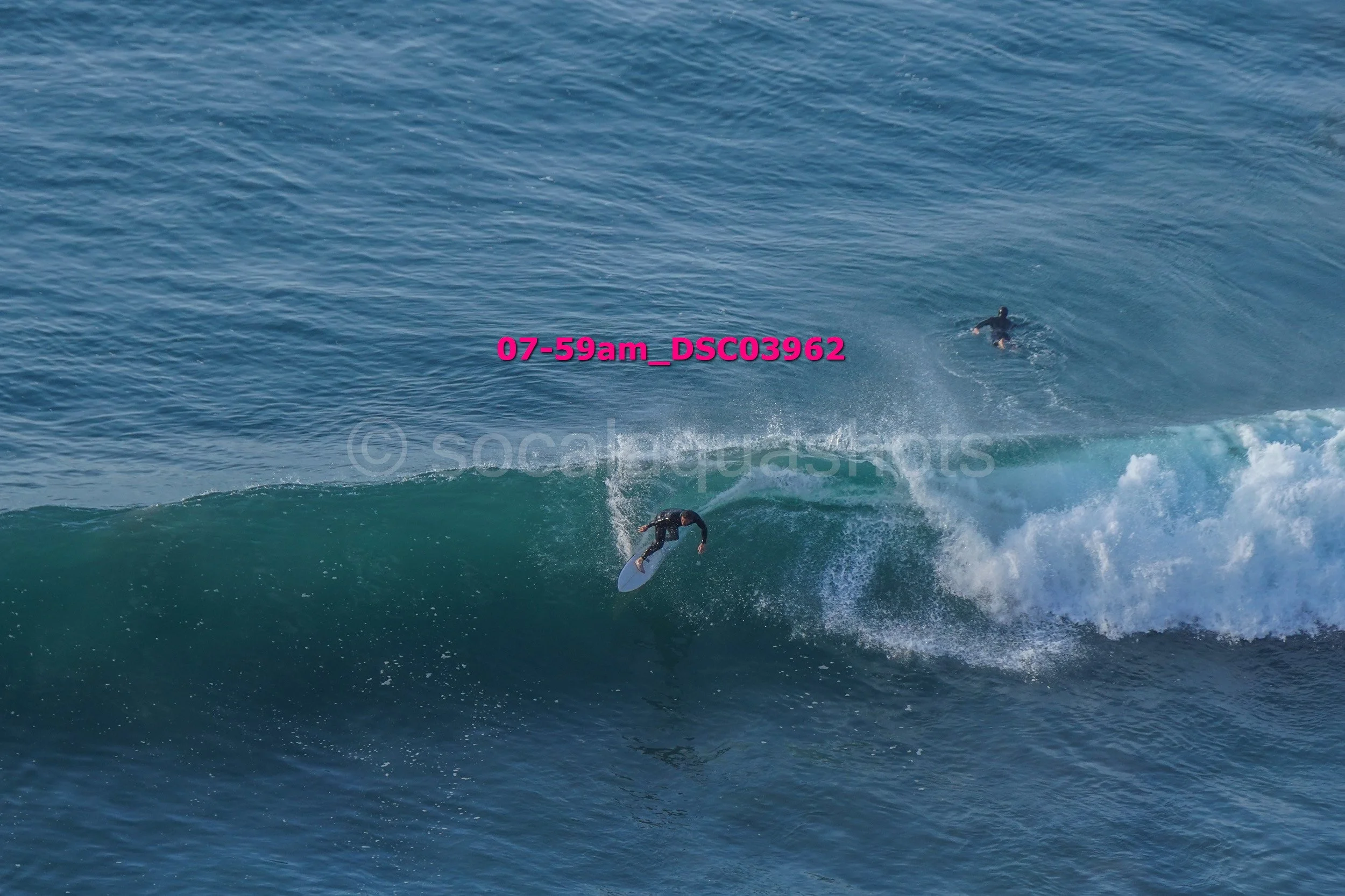 A person surfing on a wave in the ocean with another person swimming in the water nearby.