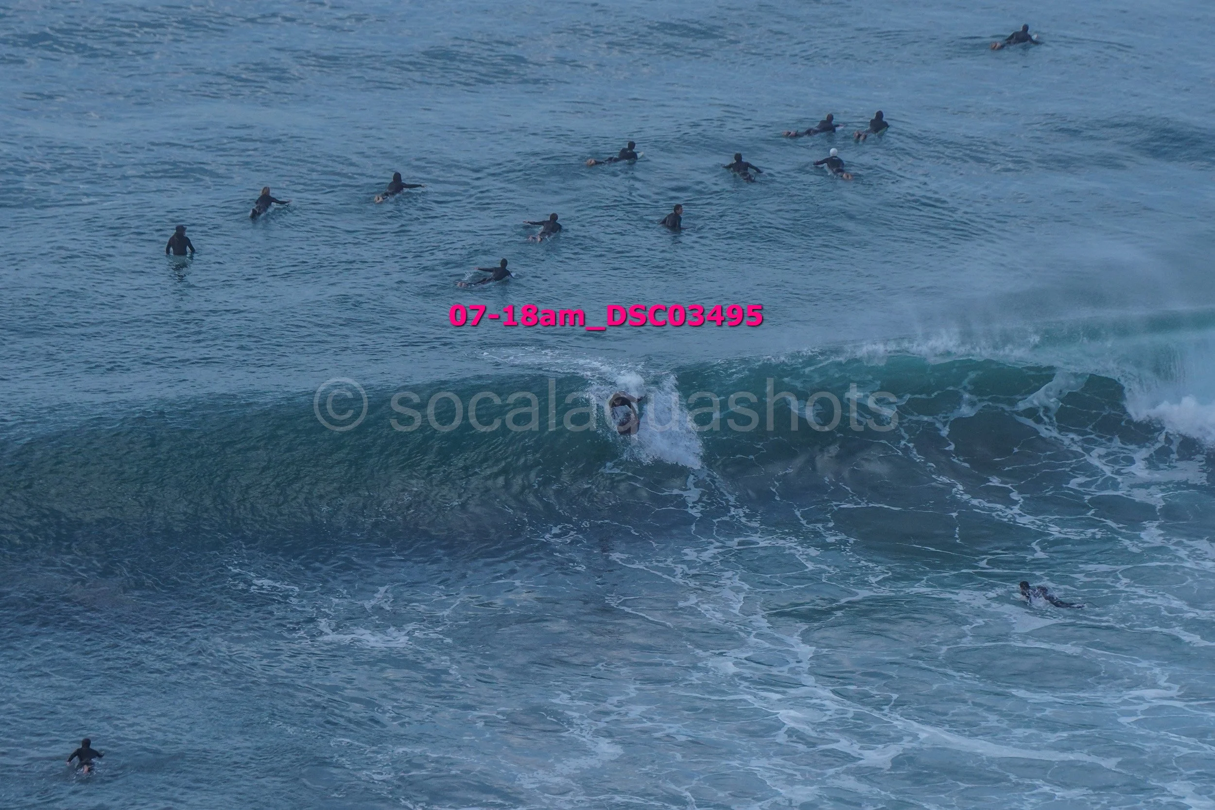 Surfer riding a wave with several people swimming and floating in the ocean in the background.
