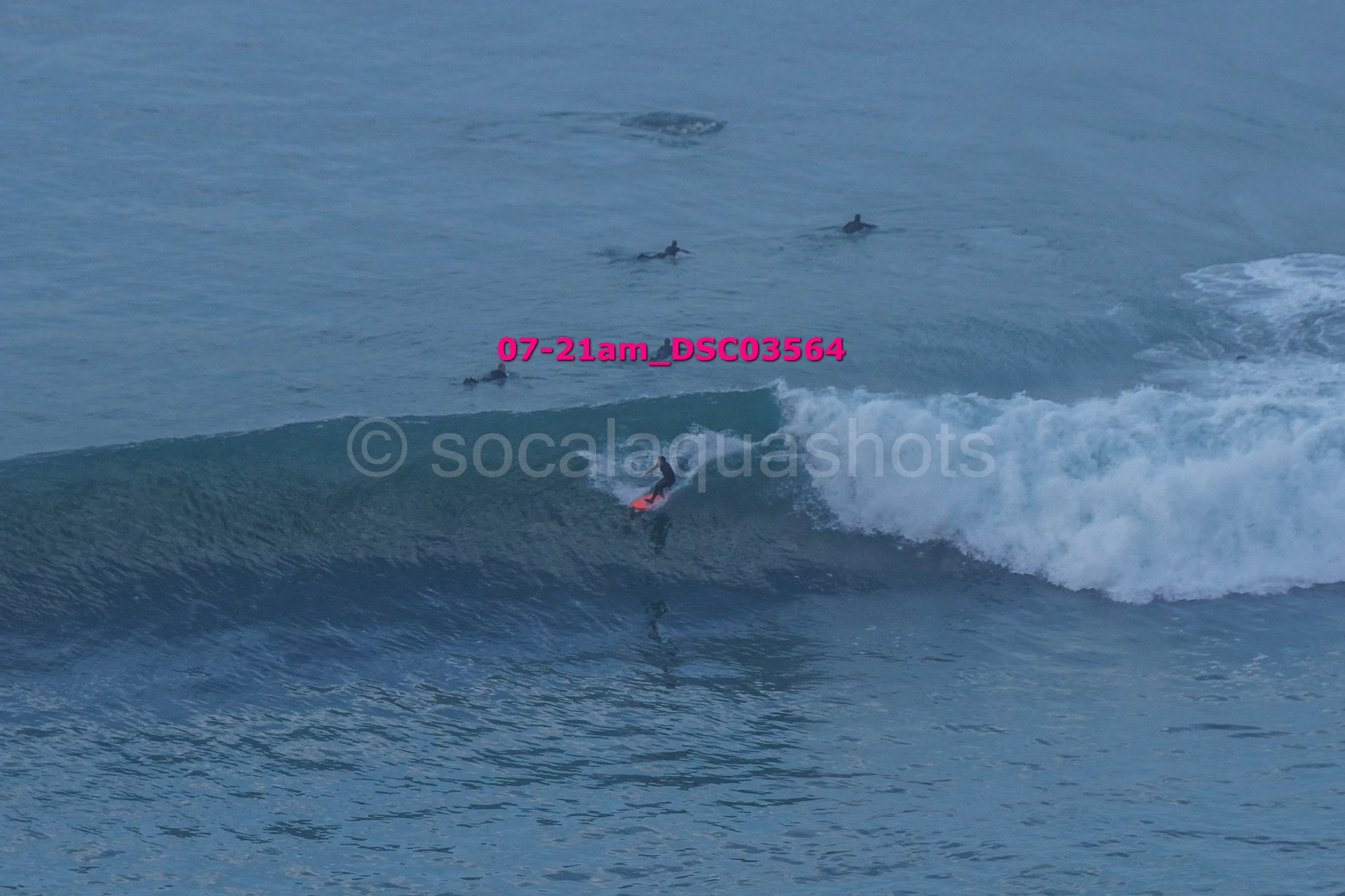 A person surfing on a wave in the ocean, with several others in the water in the background.