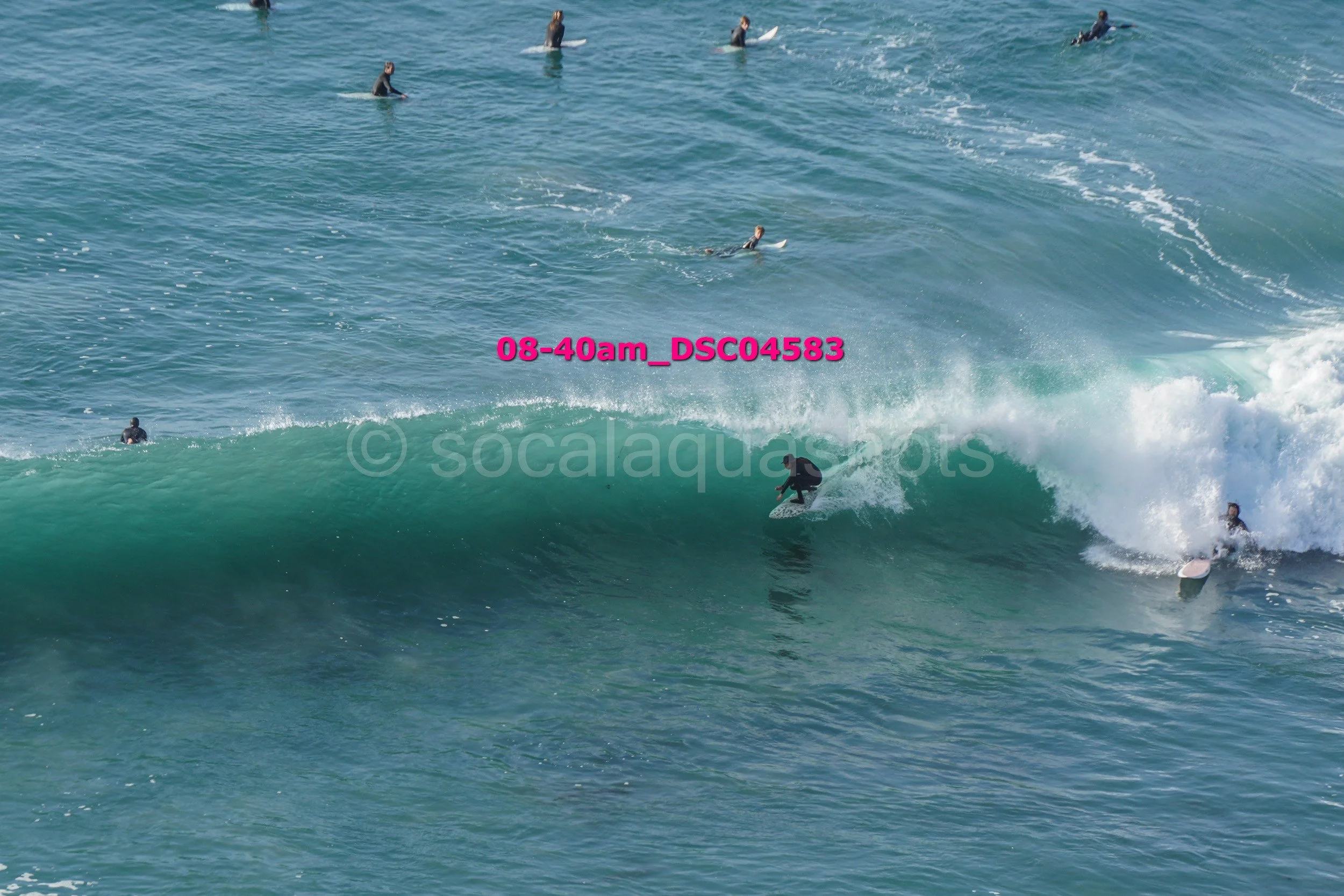 A group of surfers in the ocean, some riding a wave while others wait in the water.