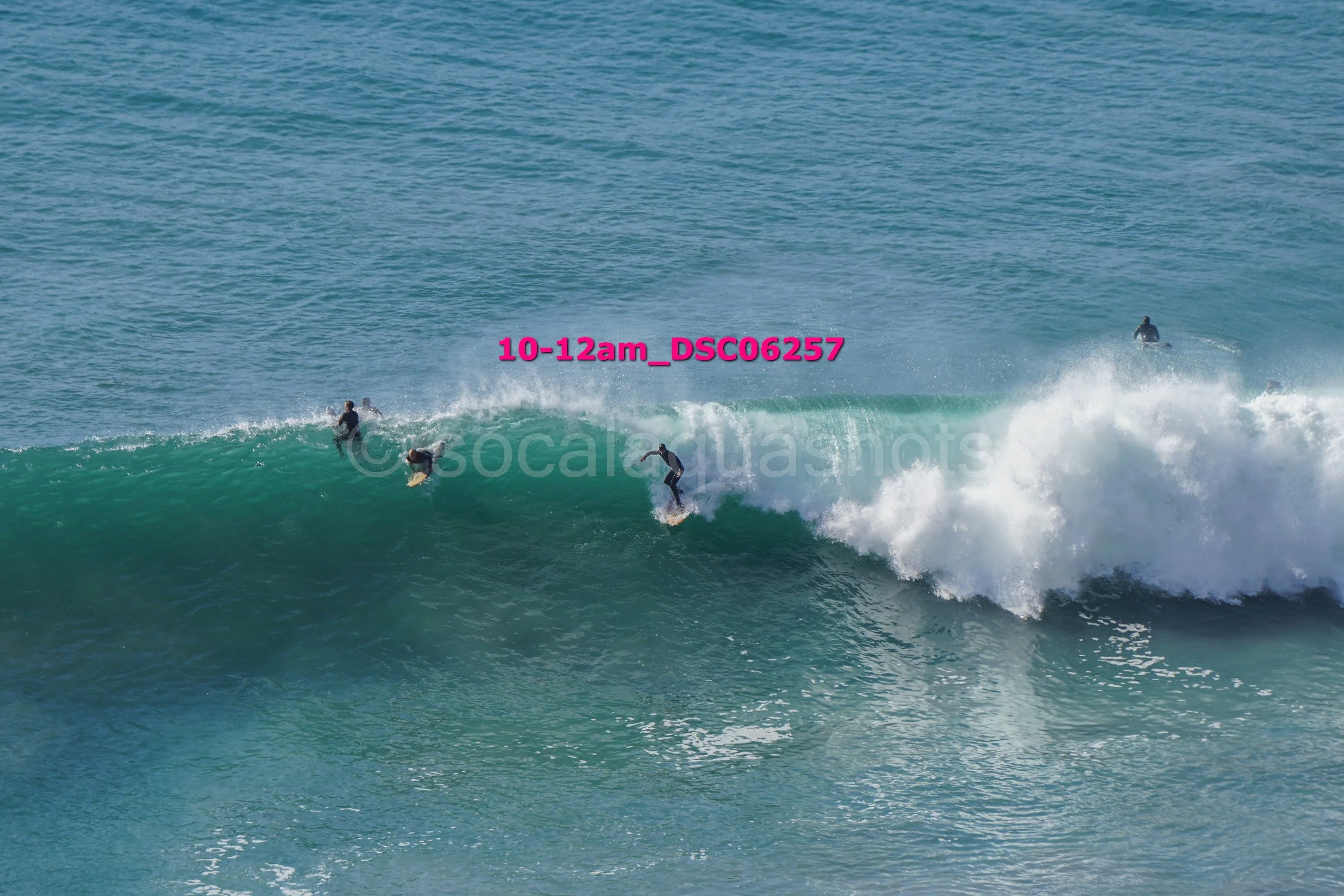 Four surfers riding and paddling on ocean waves during daytime.