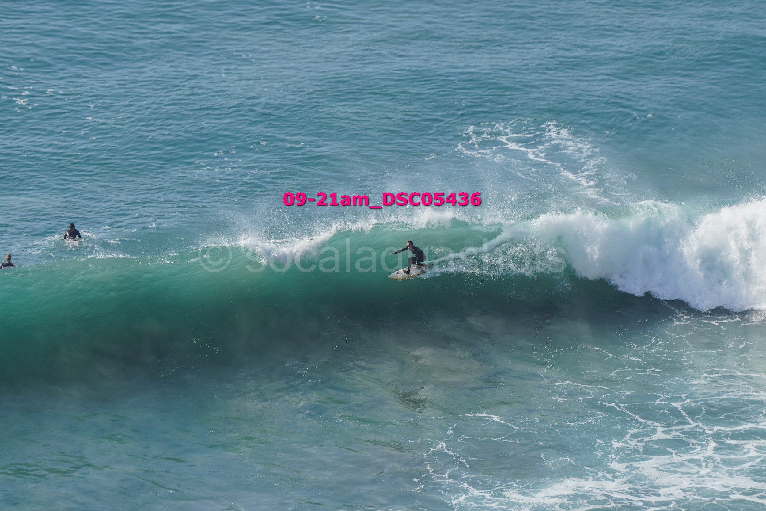 A person surfing on a wave in the ocean with two other surfers nearby.