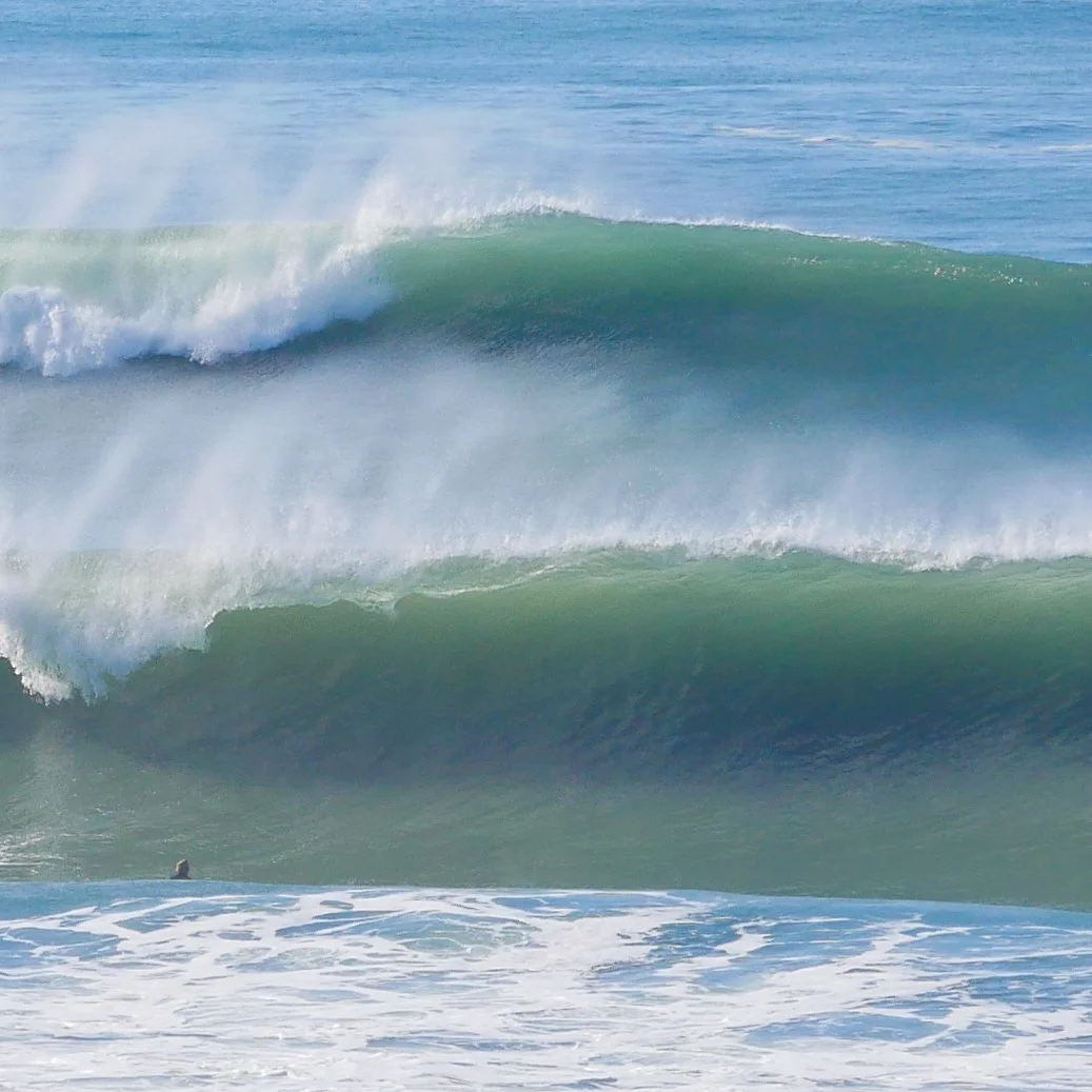 Large ocean waves with white foam, surfer in the foreground