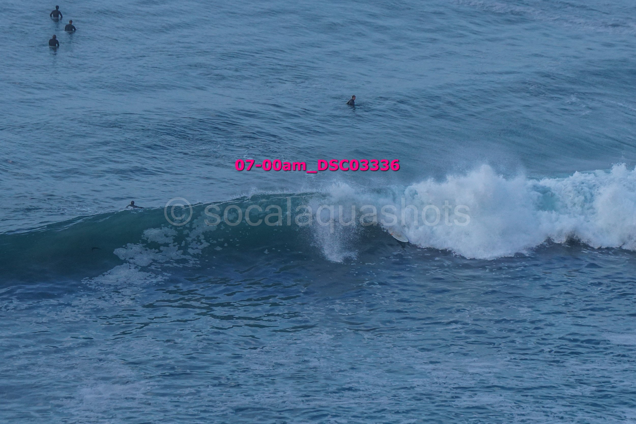 People surfing and swimming in the ocean with waves, some surfers catching a wave, a few swimmers in the water.