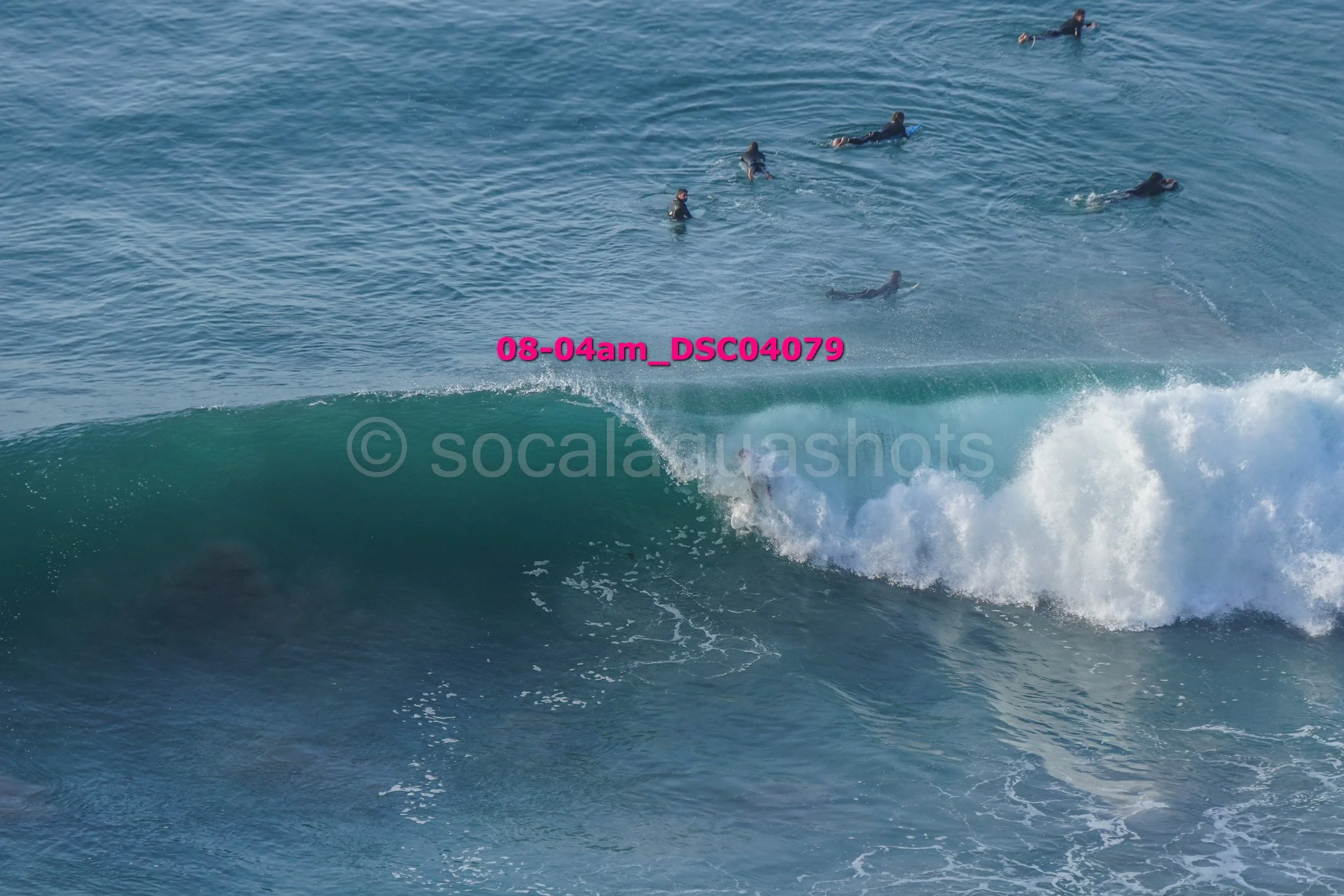 People swimming in the ocean near a large wave