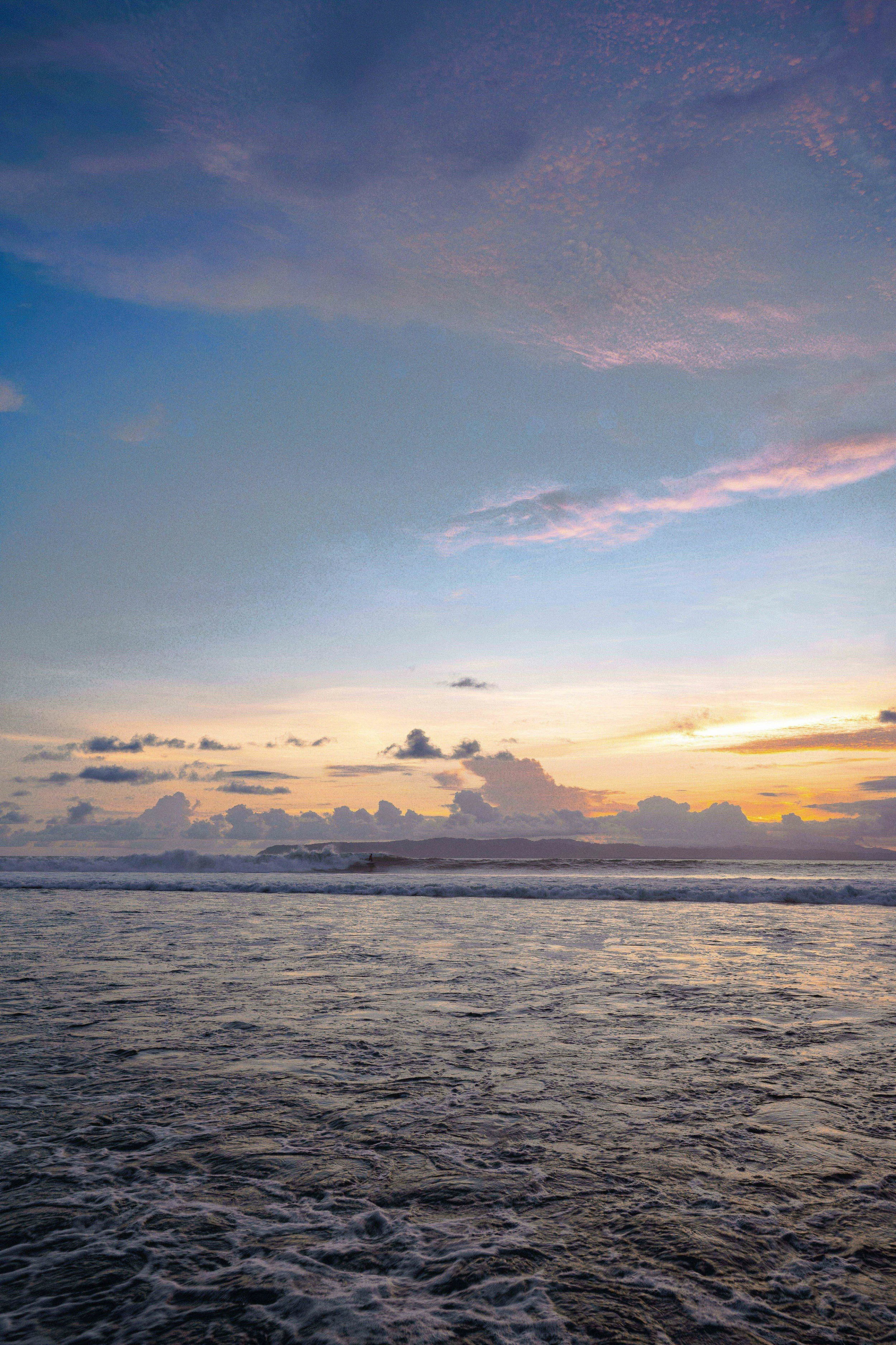 View of the ocean at sunset with visible waves and a sky with scattered pink and purple clouds.