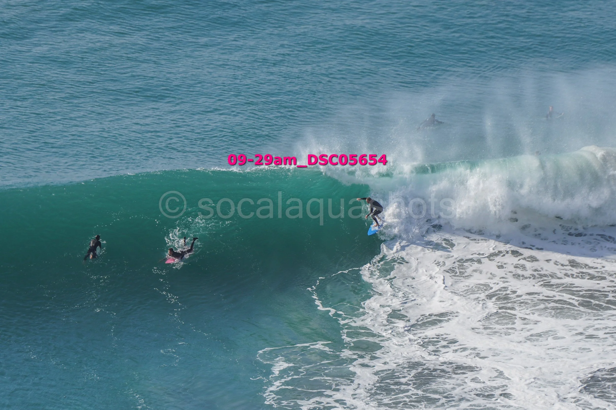 A surfer riding inside a large ocean wave while three other surfers paddling in the water nearby