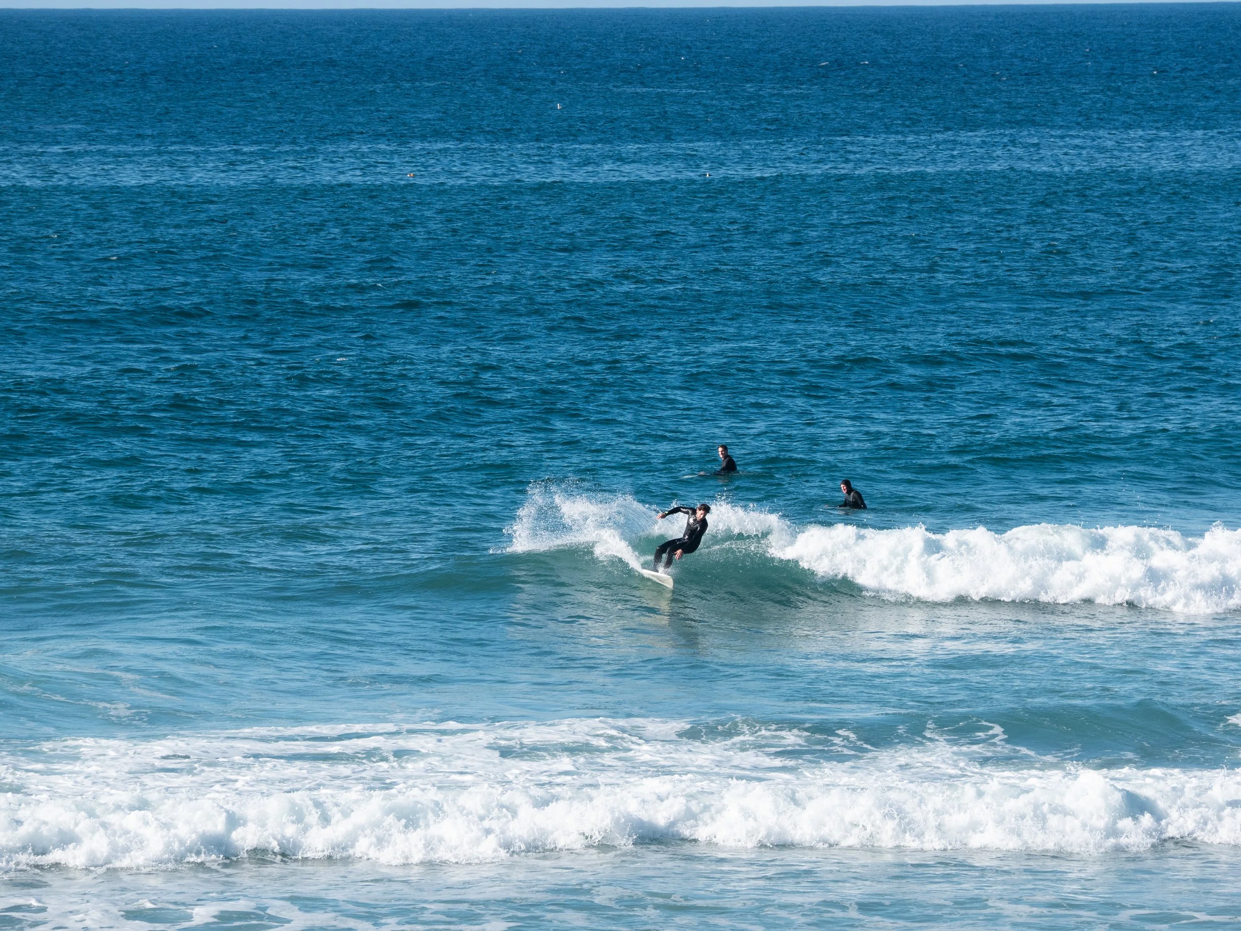 A person surfing on a wave in the ocean with two other surfers in the background.