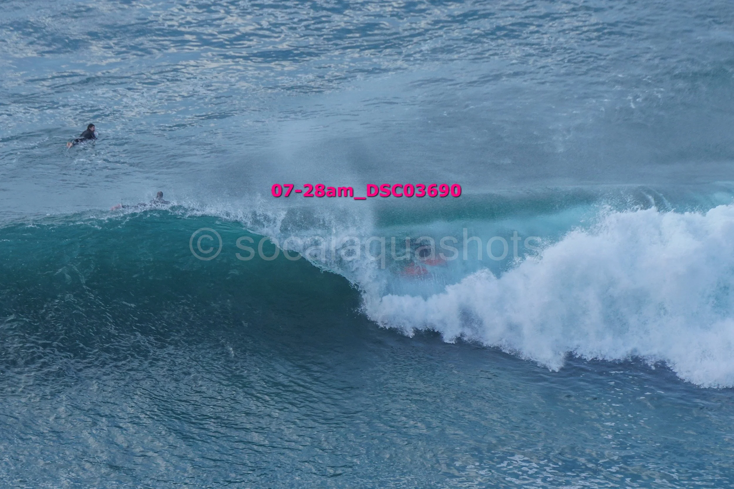 Surfer falling off a wave in the ocean with two other surfers visible in the background.