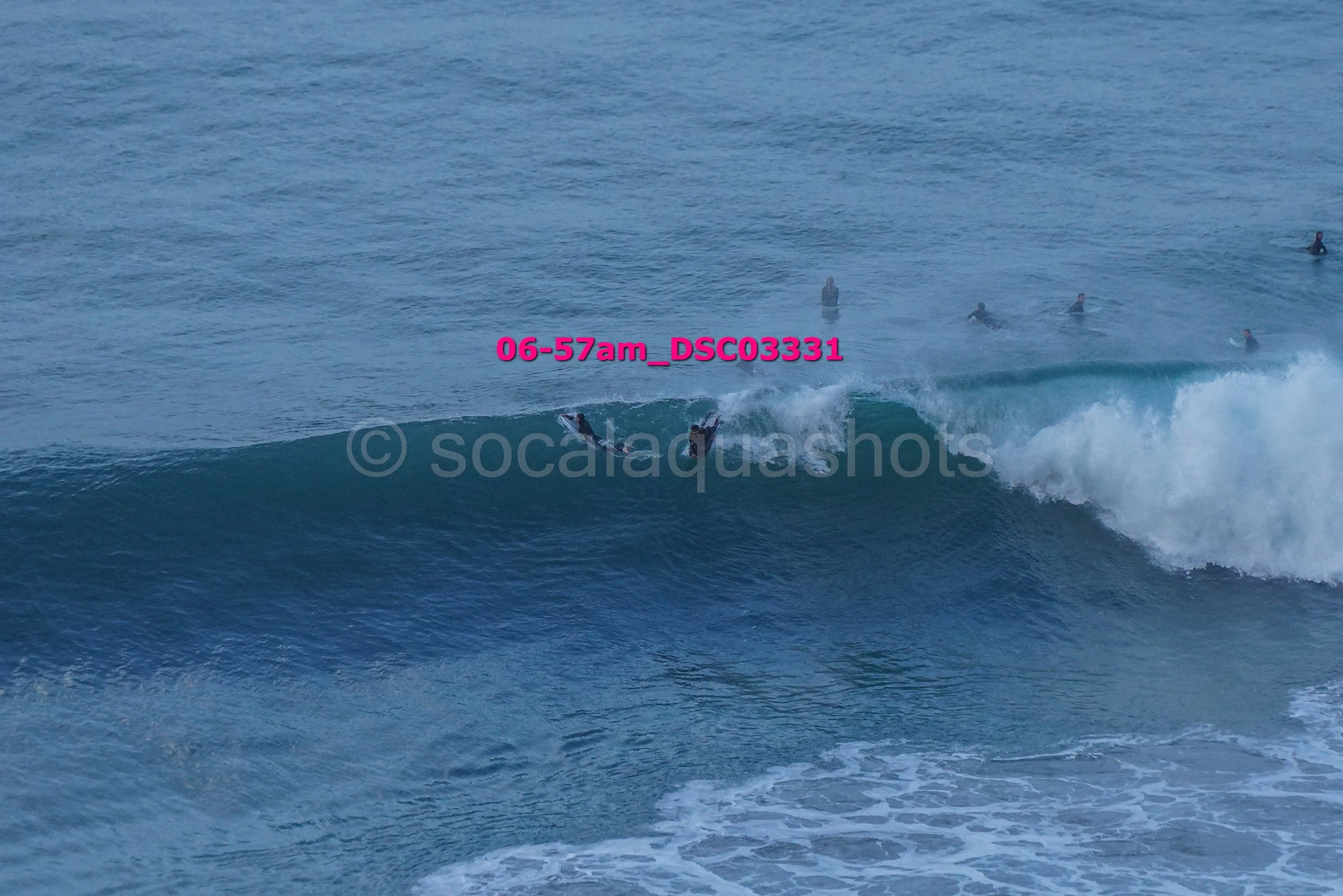A group of surfers in the ocean, one riding a wave with others waiting in the water.