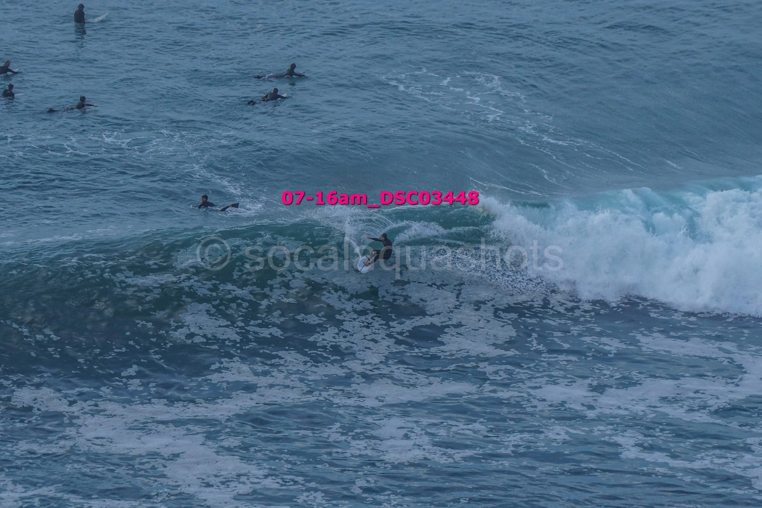 A group of surfers in the ocean, with one surfer riding a wave while others wait in the water.