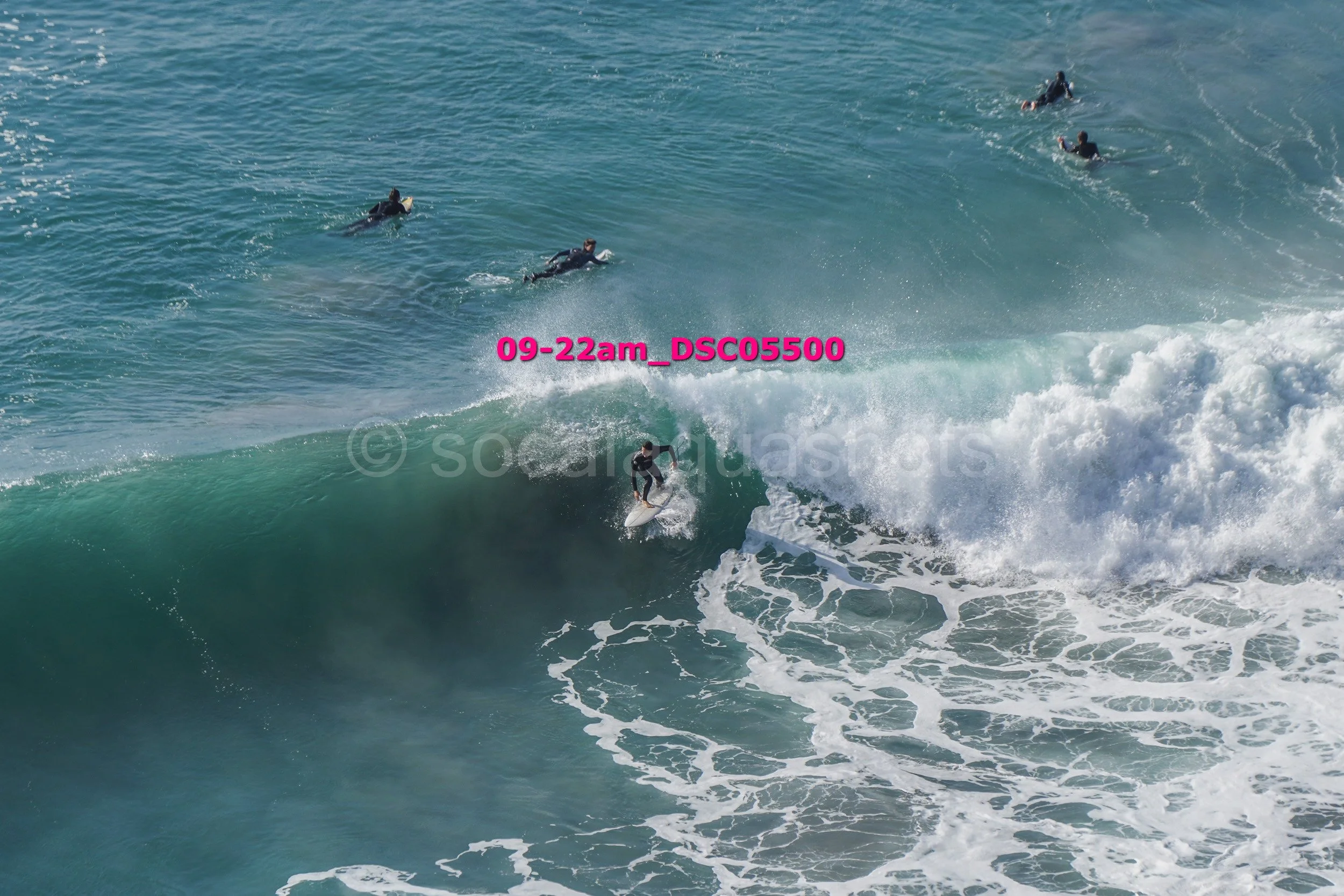 A person surfing on a large wave with four other surfers in the water nearby.