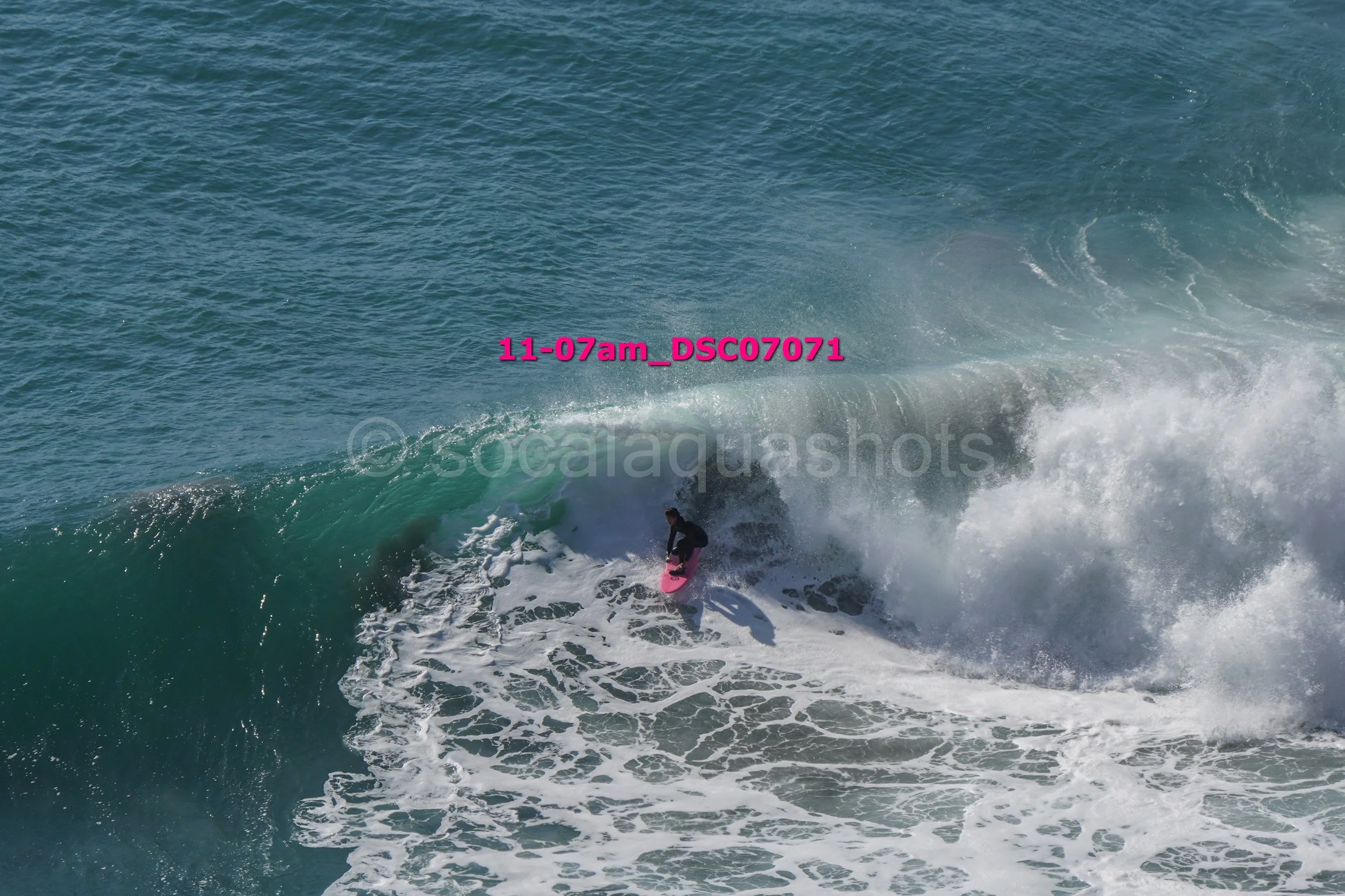 A person surfing on a pink surfboard on a large ocean wave.