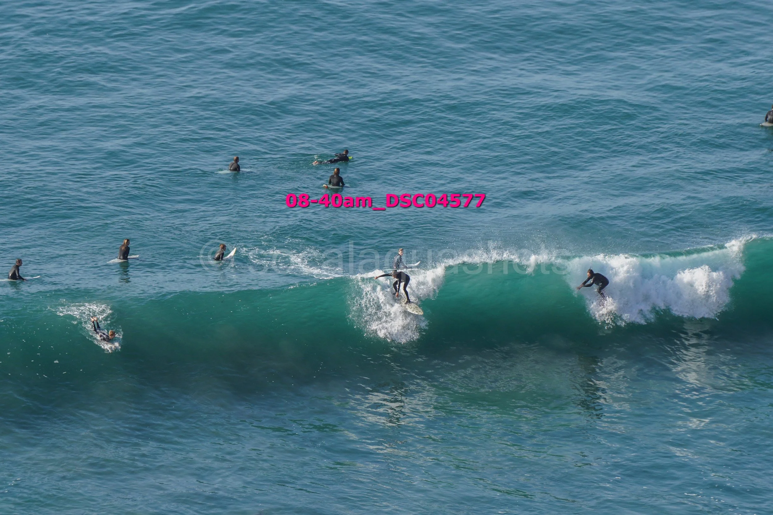 A group of surfers in wetsuits riding and waiting on a large ocean wave.