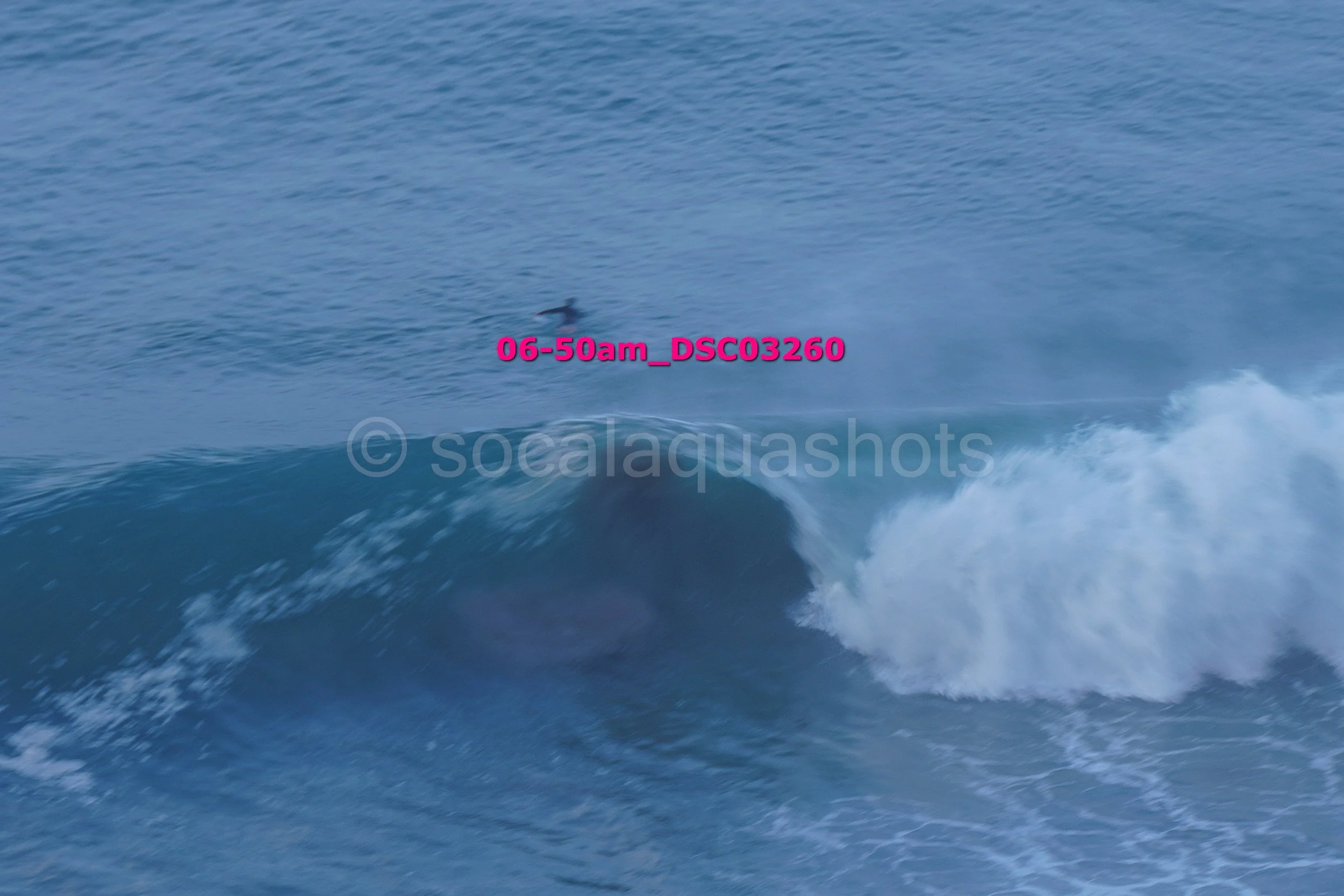 A person surfing on a large ocean wave during daylight. The wave is breaking, and the surfer is near the top, riding the crest.