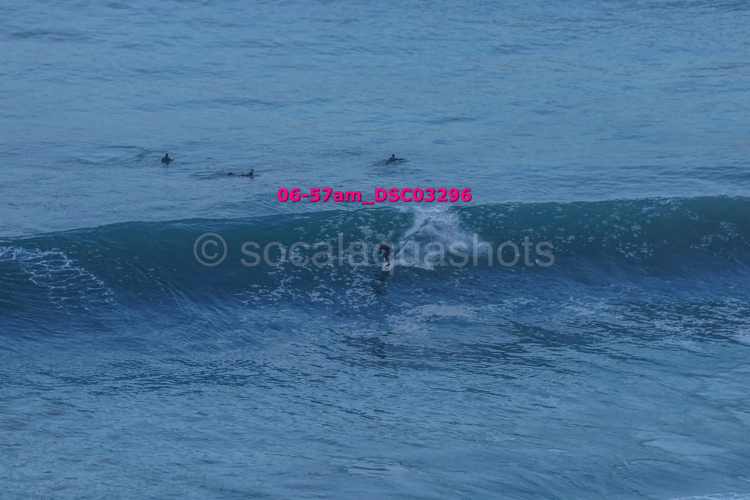 A person is surfing on a wave in the ocean with three other surfers visible in the background.