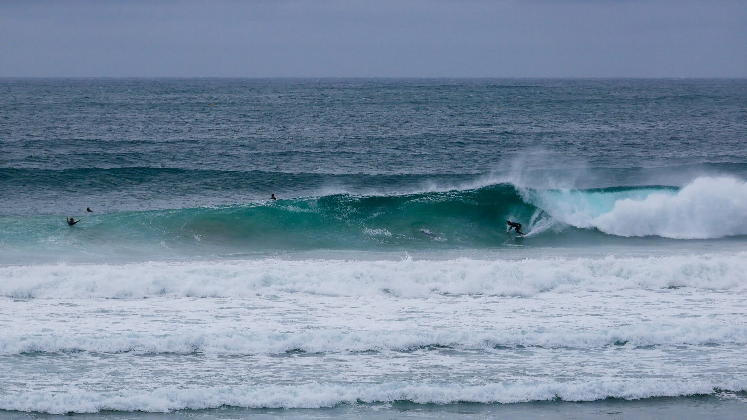 Surfer riding wave in ocean with other surfers nearby.
