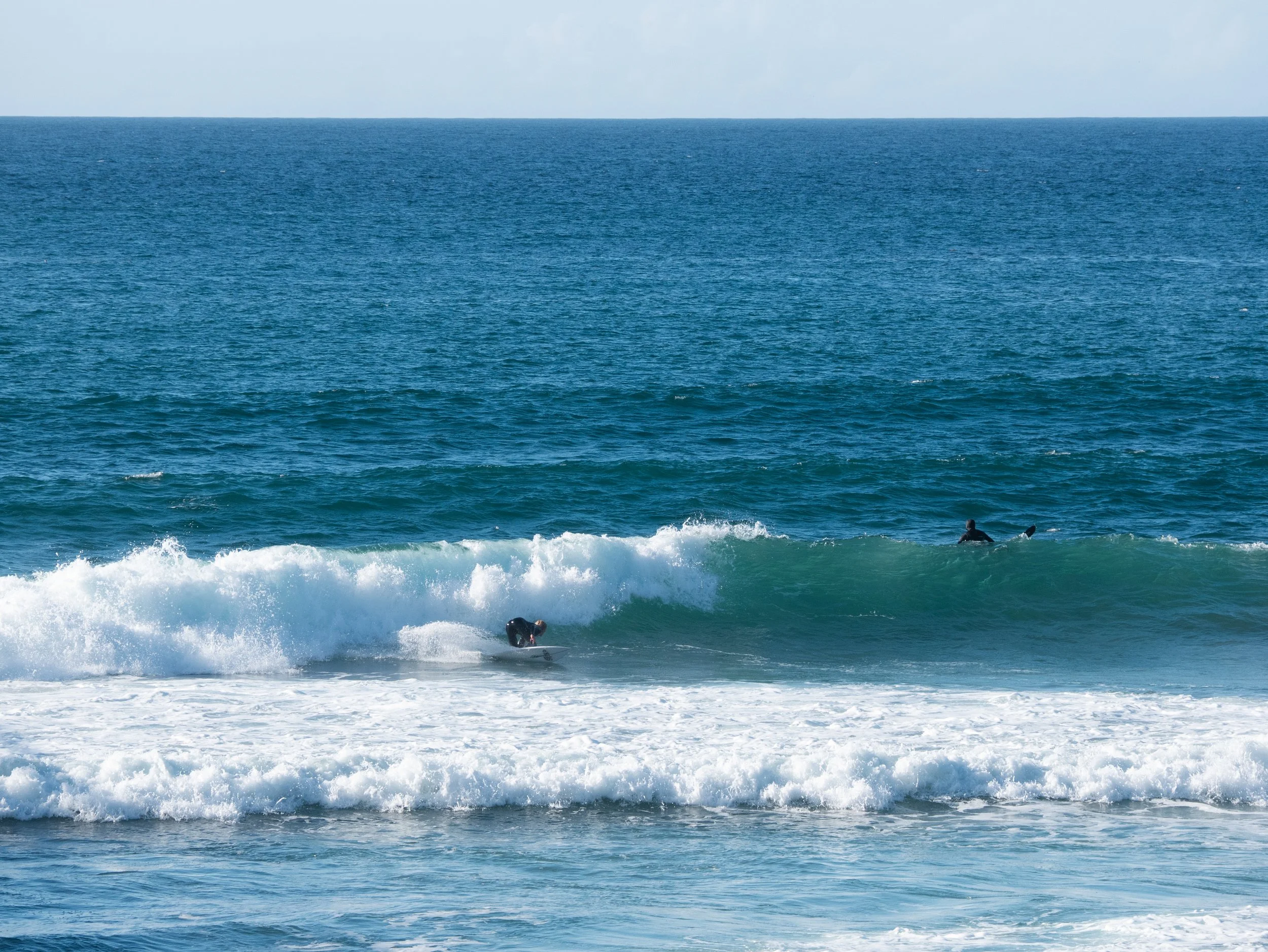 Surfer riding a wave in the ocean with another surfer paddling in the background.