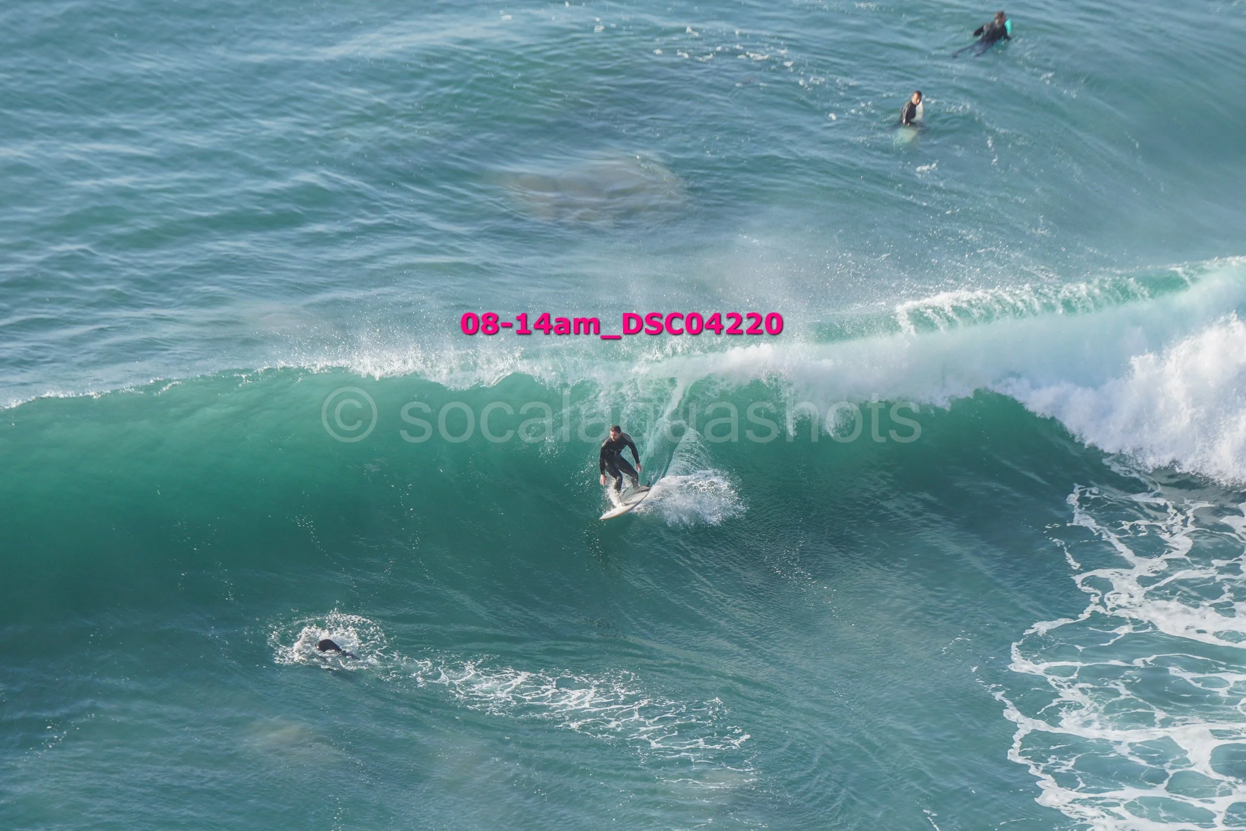 Surfer riding a large wave with two other surfers in the water nearby in the ocean.