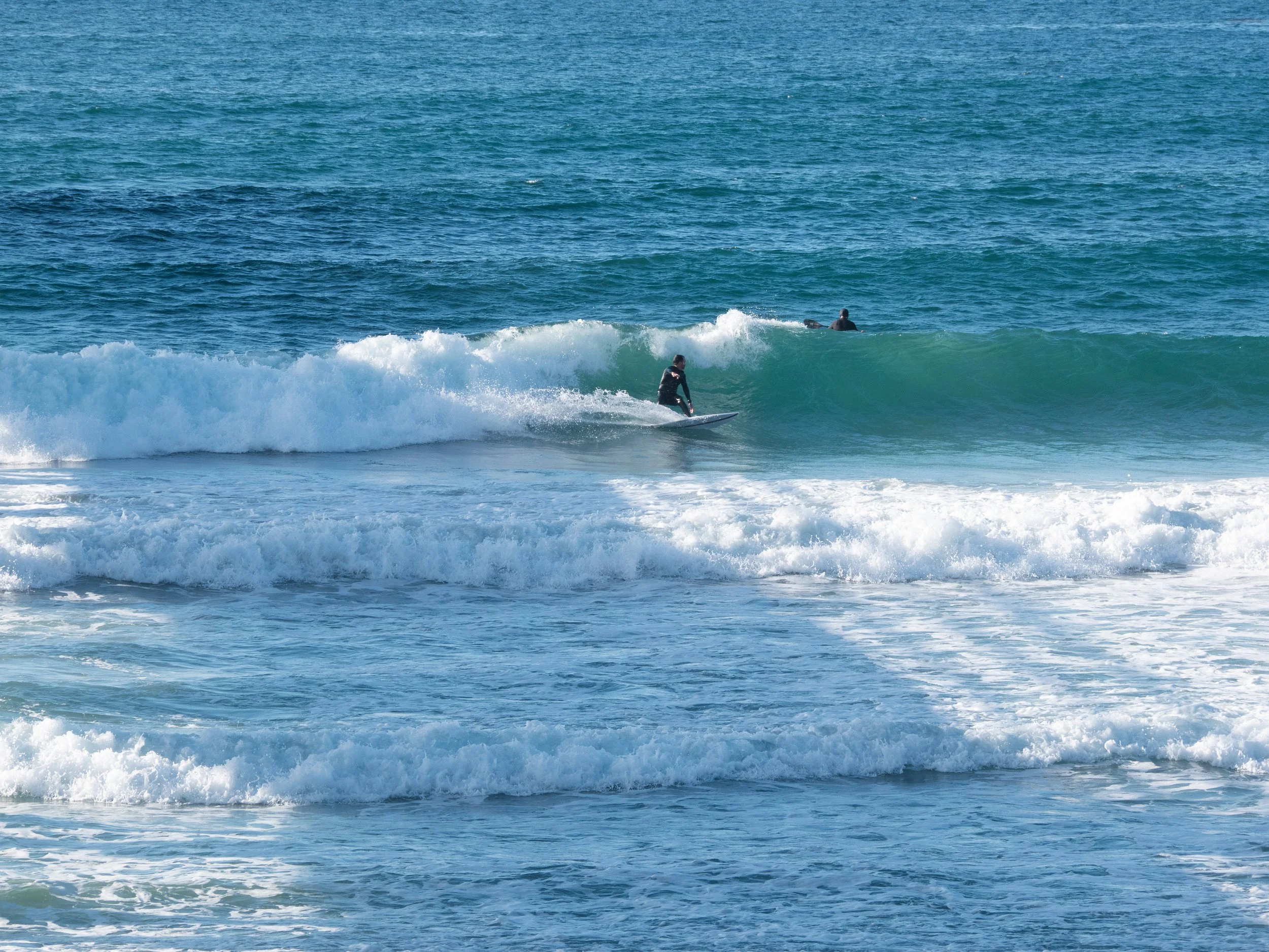 Two surfers riding waves at the beach with the ocean in the background.