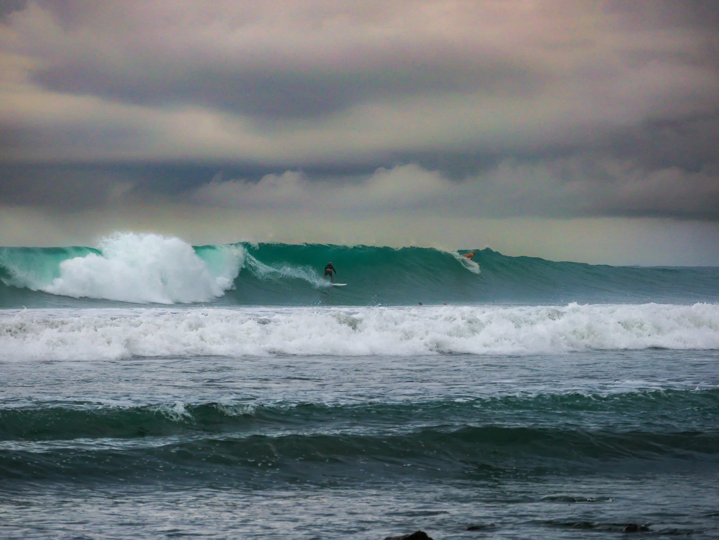 Surfer riding a large ocean wave under cloudy skies
