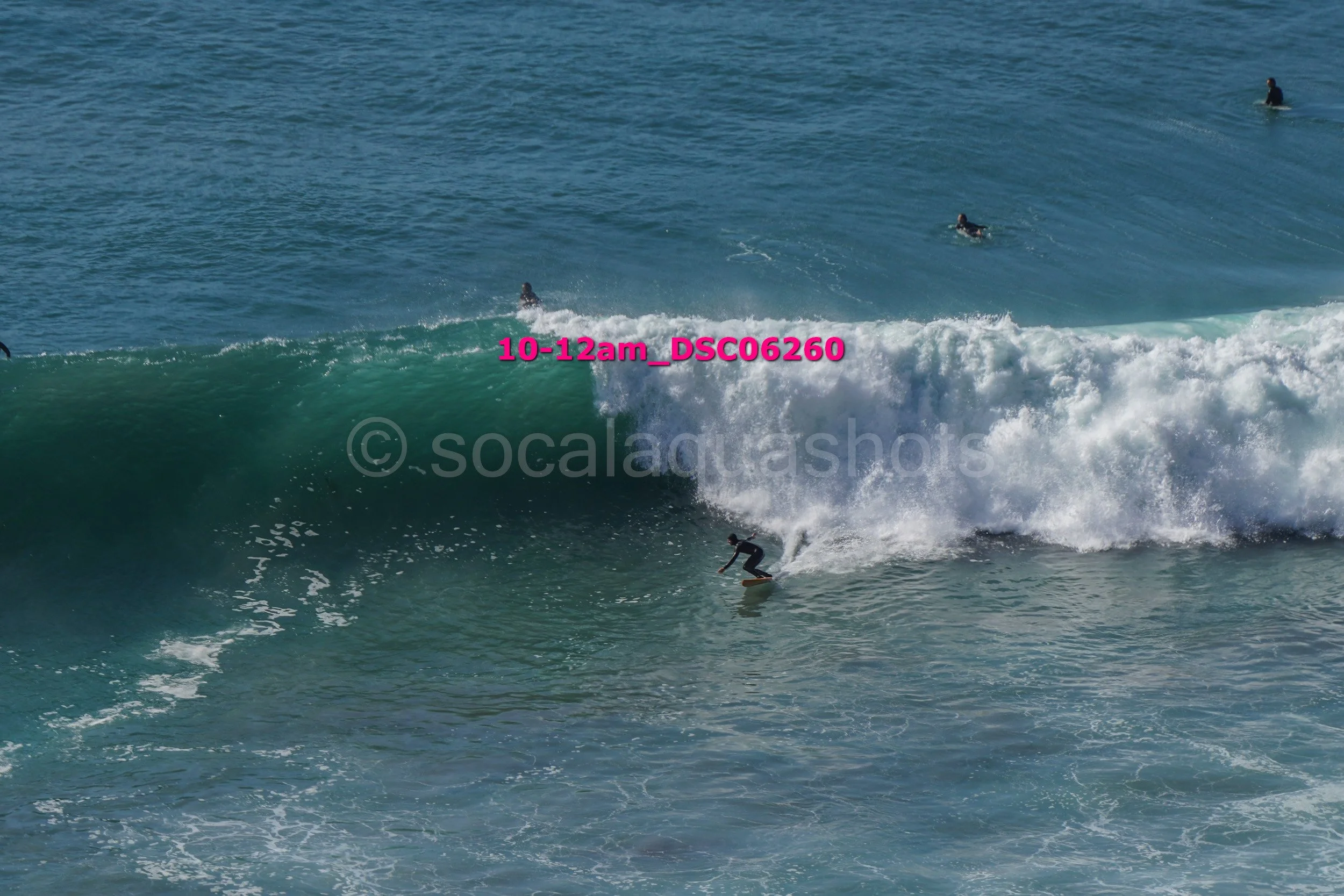 A surfer riding a wave in the ocean with several other surfers in the water.