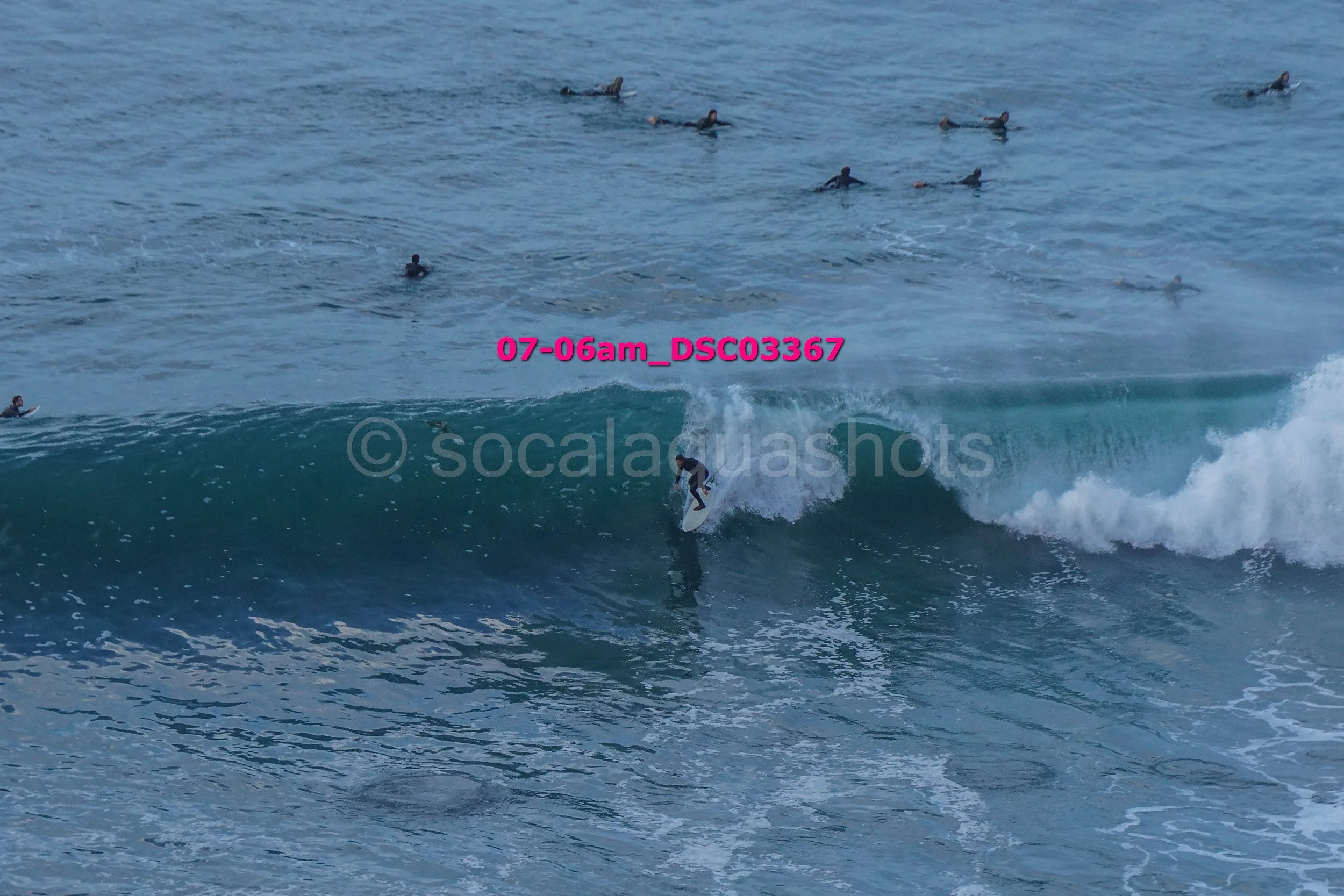 A person surfing on a wave with multiple surfers in the water in the background.