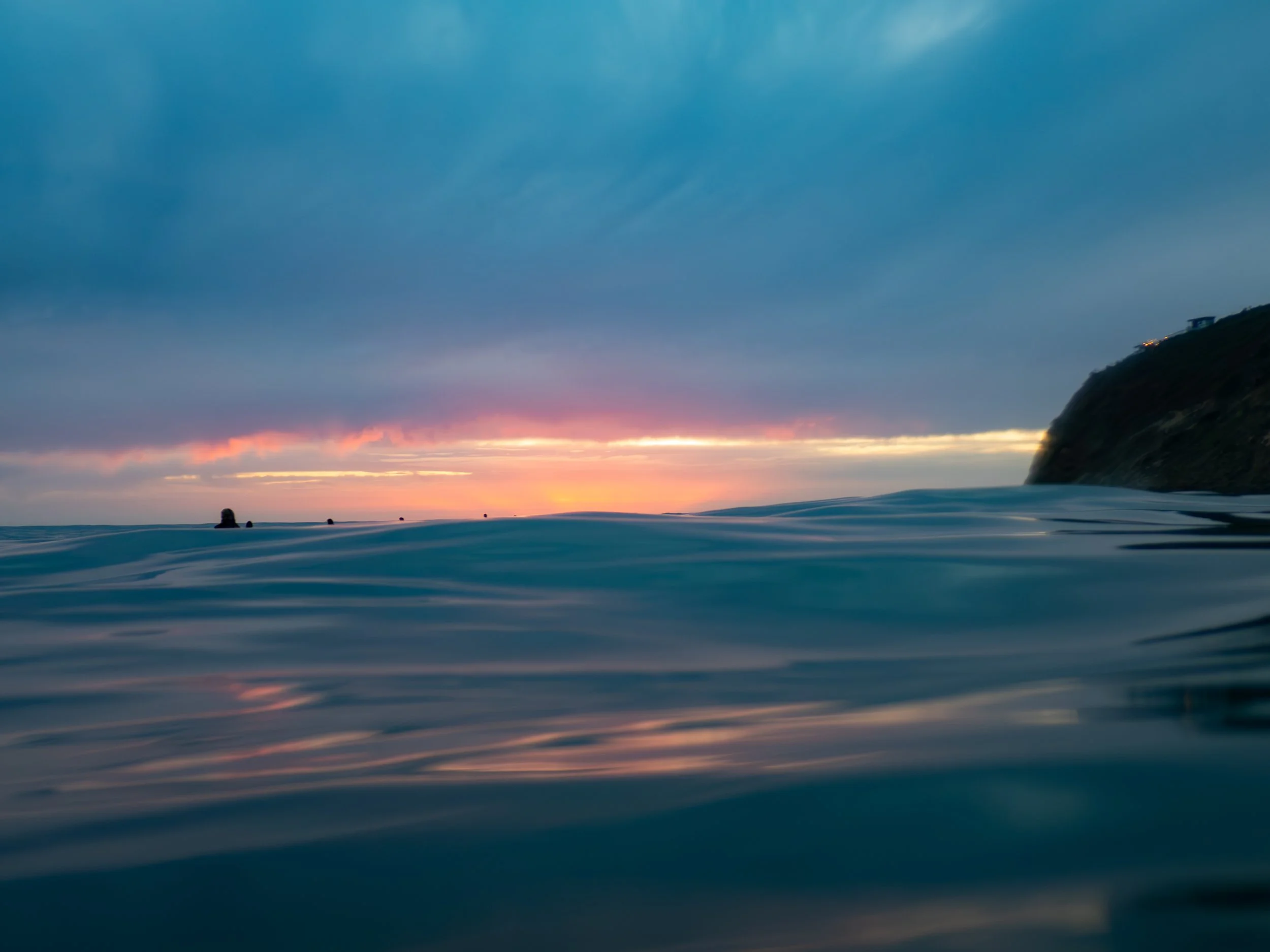 Ocean water during sunset with a distant shoreline and a cloudy sky.