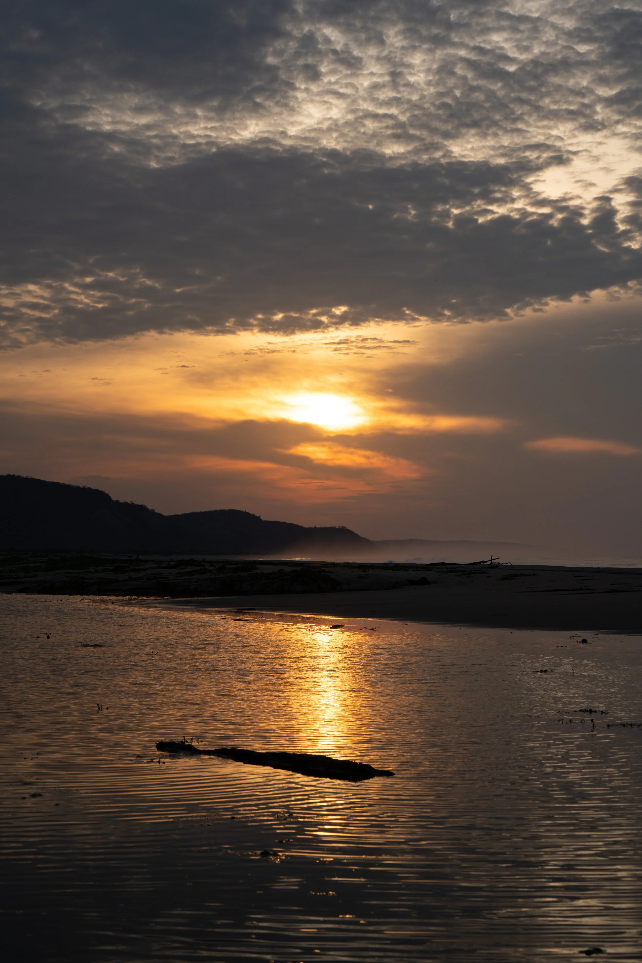 Sunset over a river with silhouettes of hills and clouds, golden reflections on the water