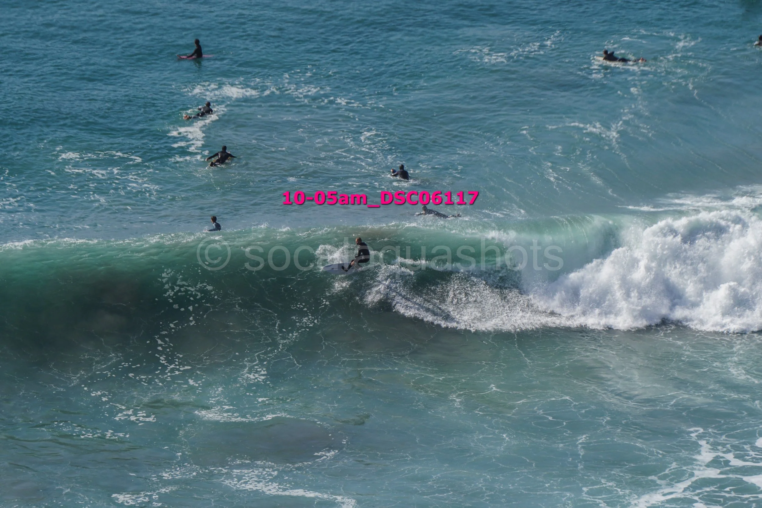 Multiple surfers riding and waiting for waves in the ocean during daytime.