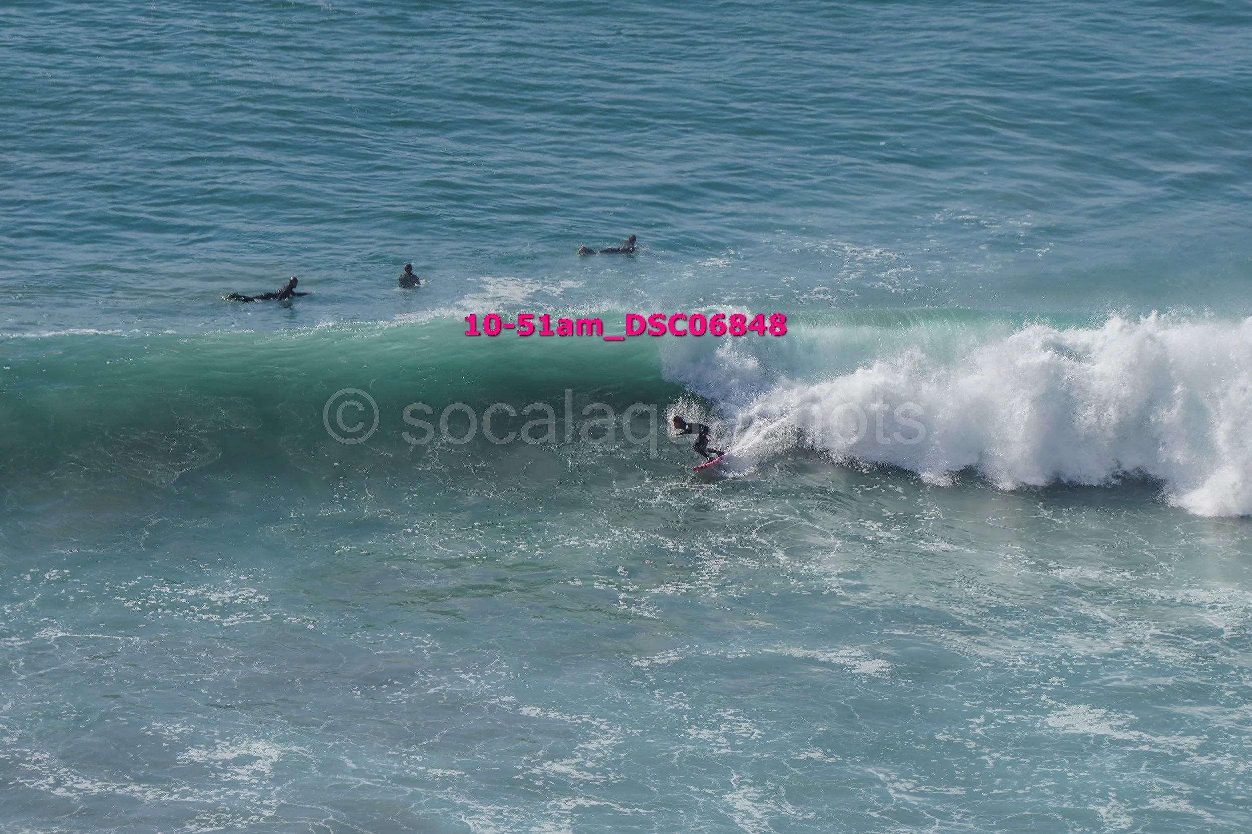Surfer riding a large wave while three others are paddling in the ocean in the background.