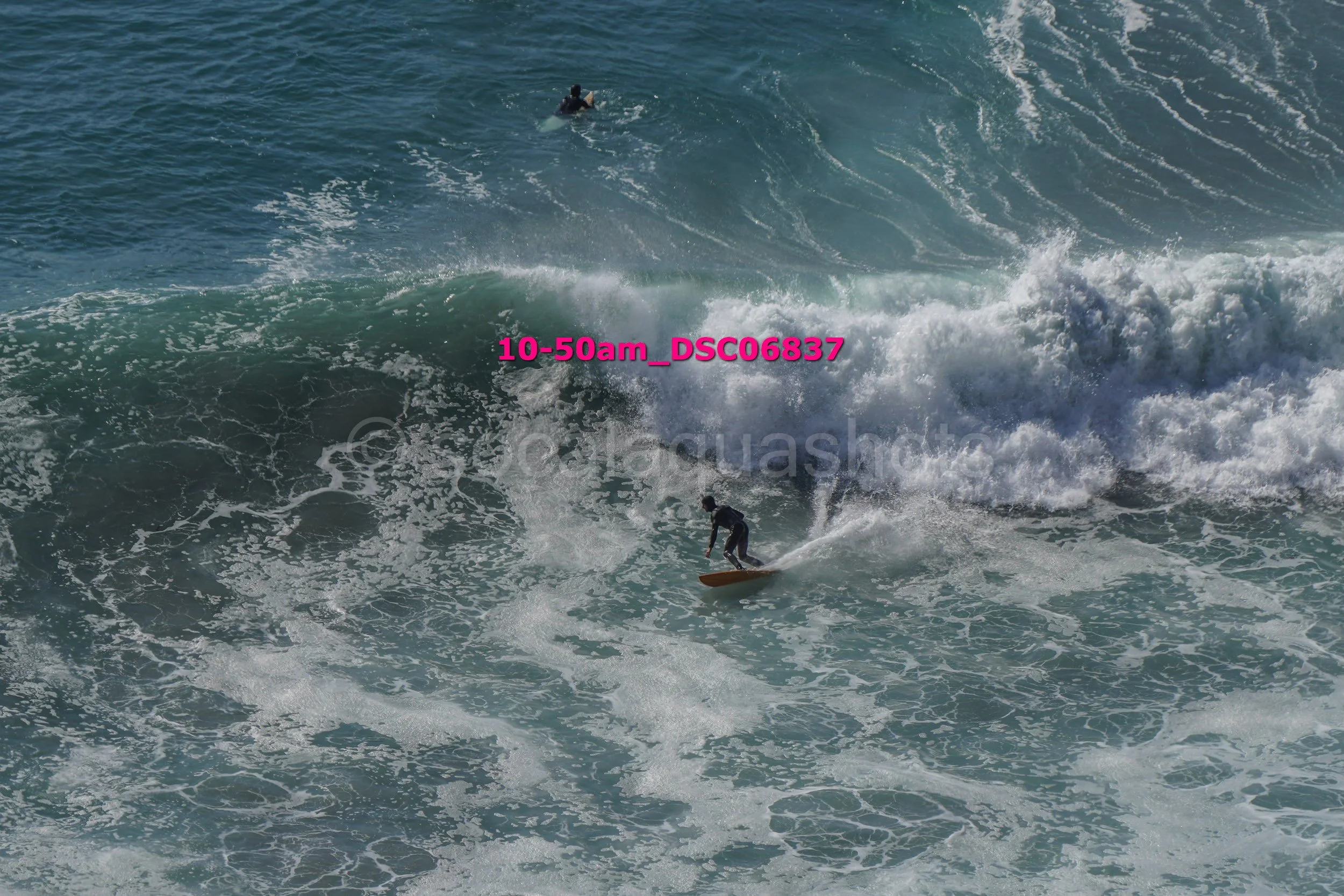 A person surfing on a large wave with an ocean in the background.