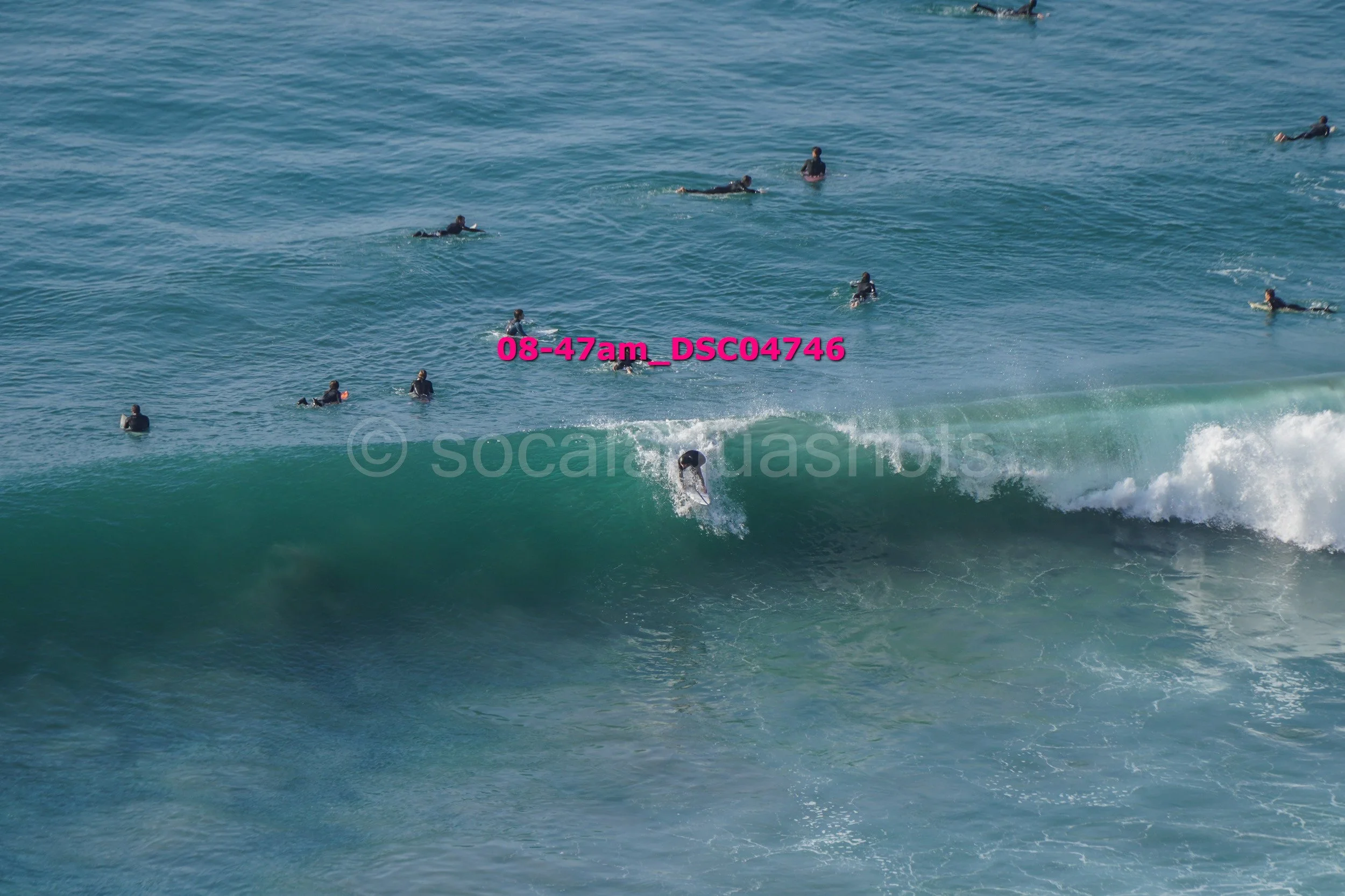 Surfer riding a wave with several people in wetsuits swimming in the ocean nearby.