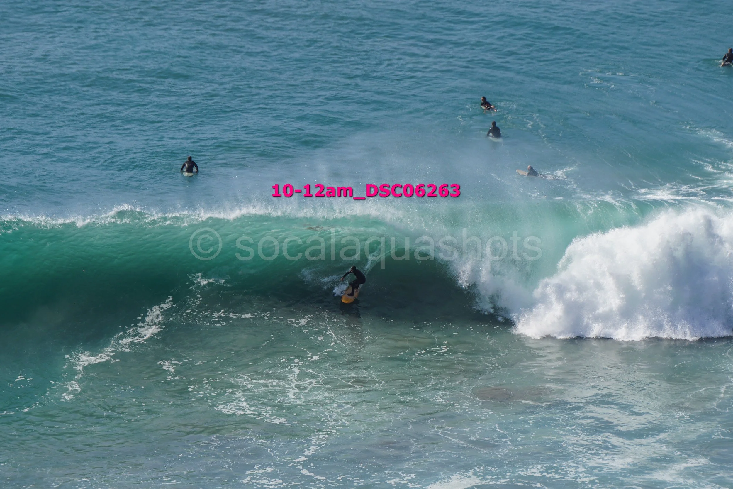A person surfing a large wave at the beach with several other surfers in the water nearby.