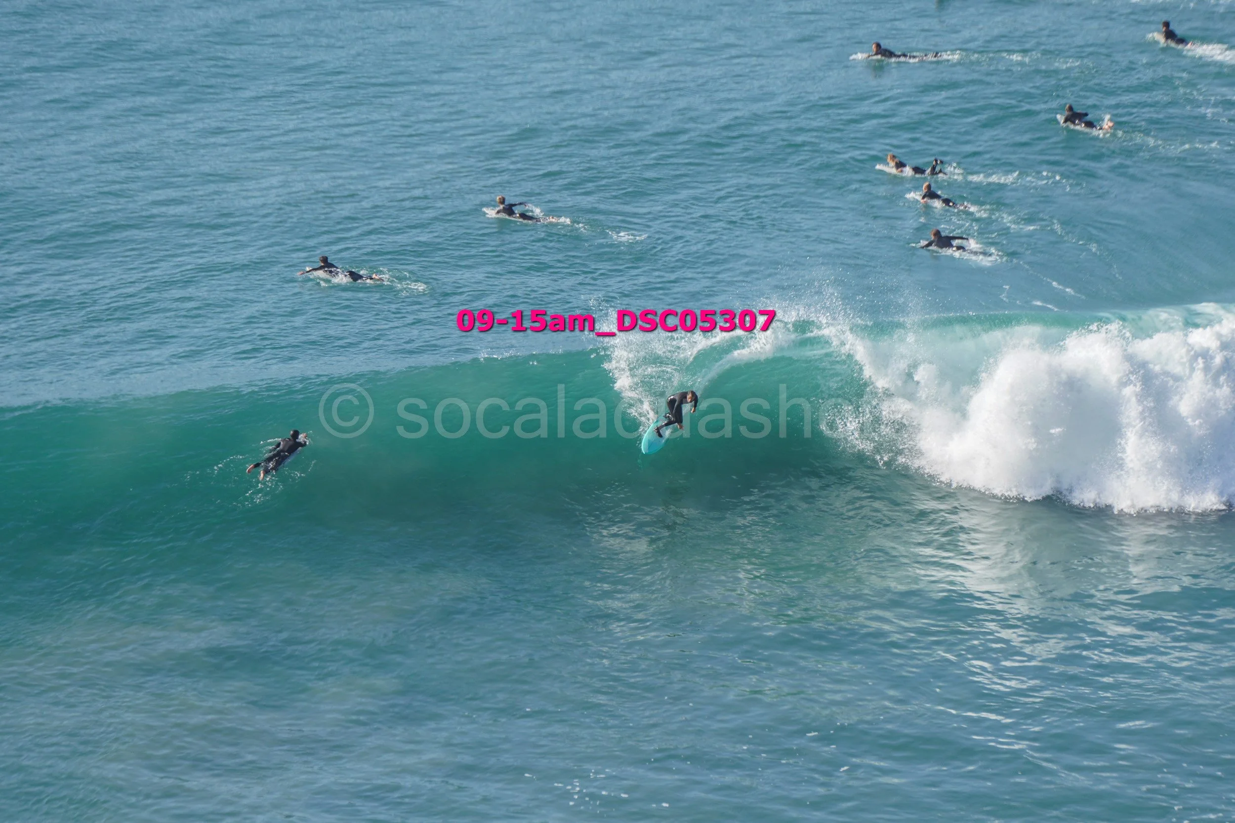 A person surfing on a wave with seven other surfers in the water nearby.