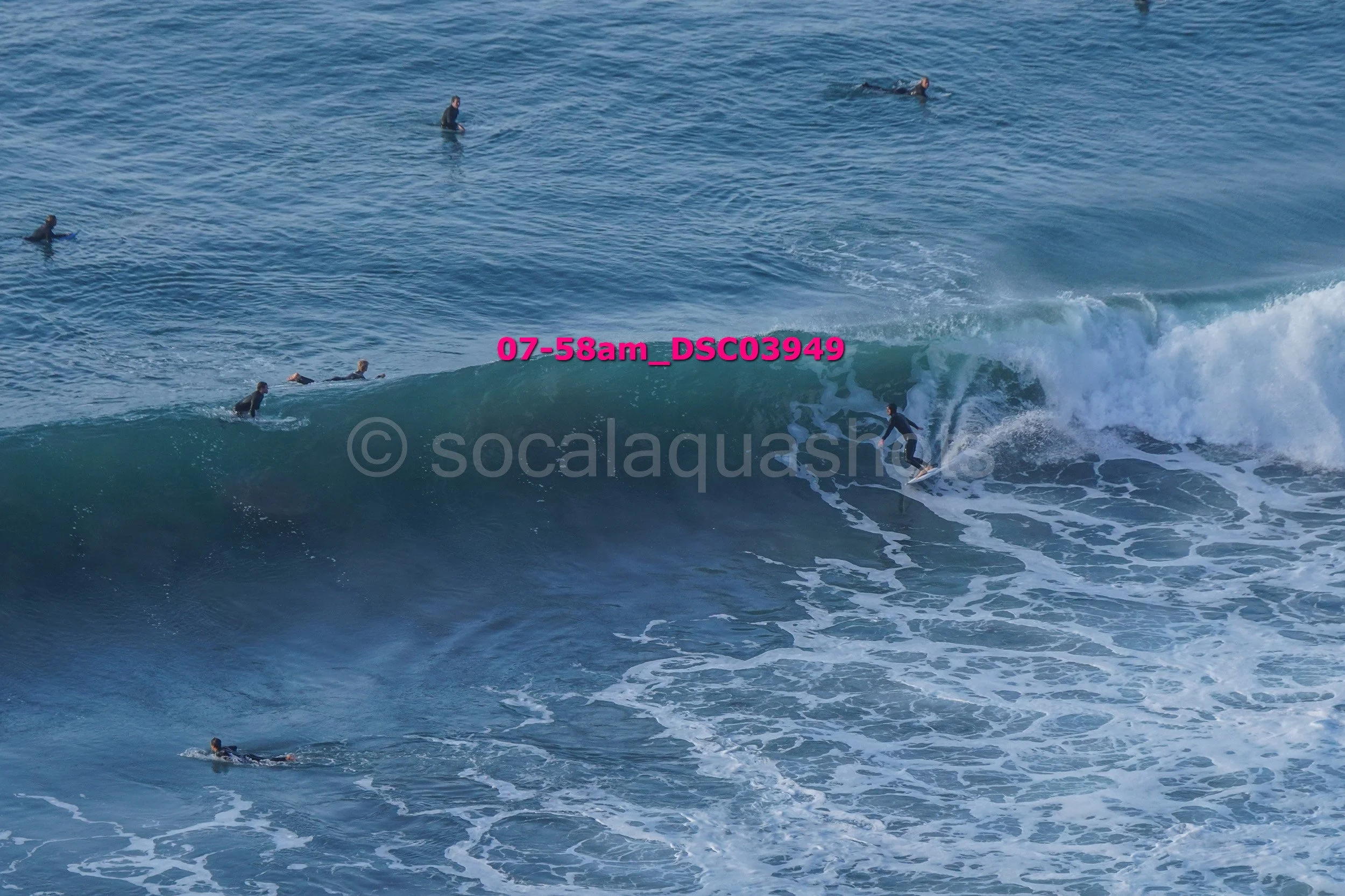 A group of surfers in wetsuits riding and waiting for waves in the ocean on a clear day.