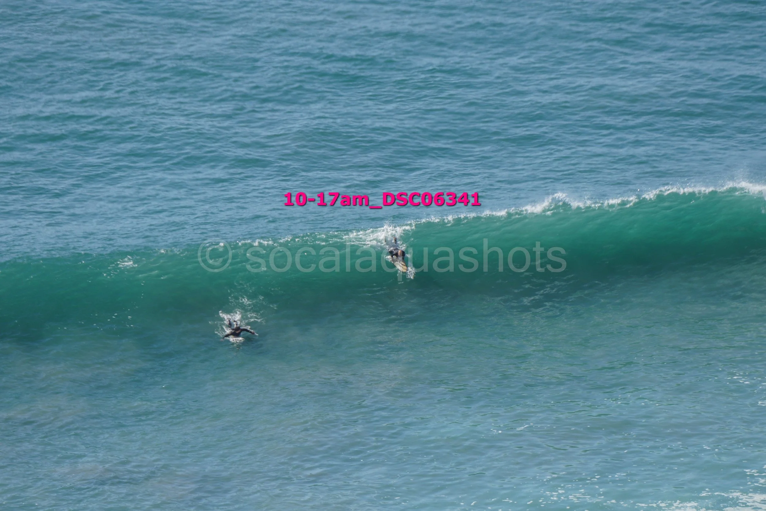 Two surfers riding a large wave in the ocean with a blue sky above.