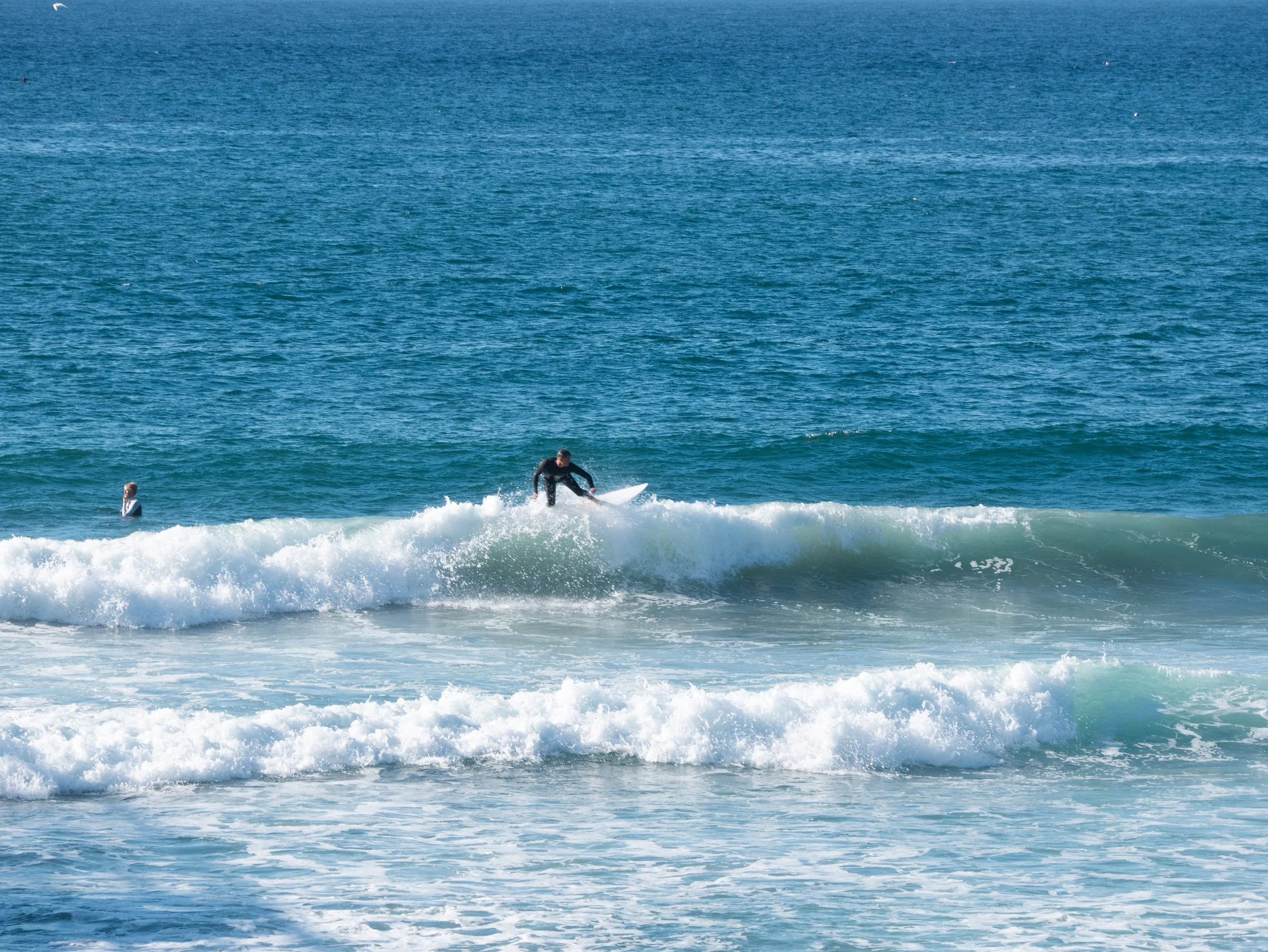 A person surfing on a wave in the ocean with another person swimming nearby.