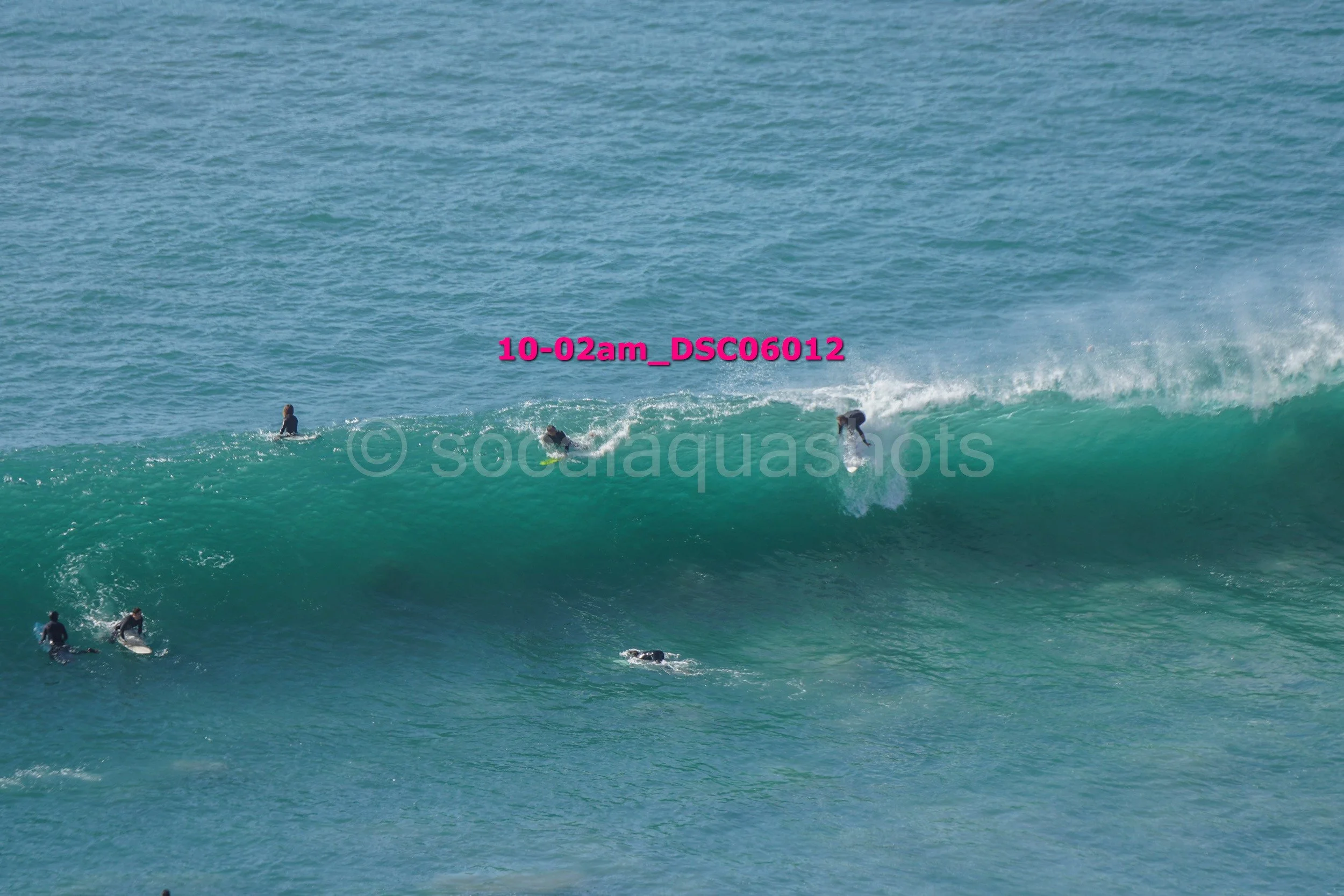 Several surfers in wetsuits riding and waiting on large ocean waves.