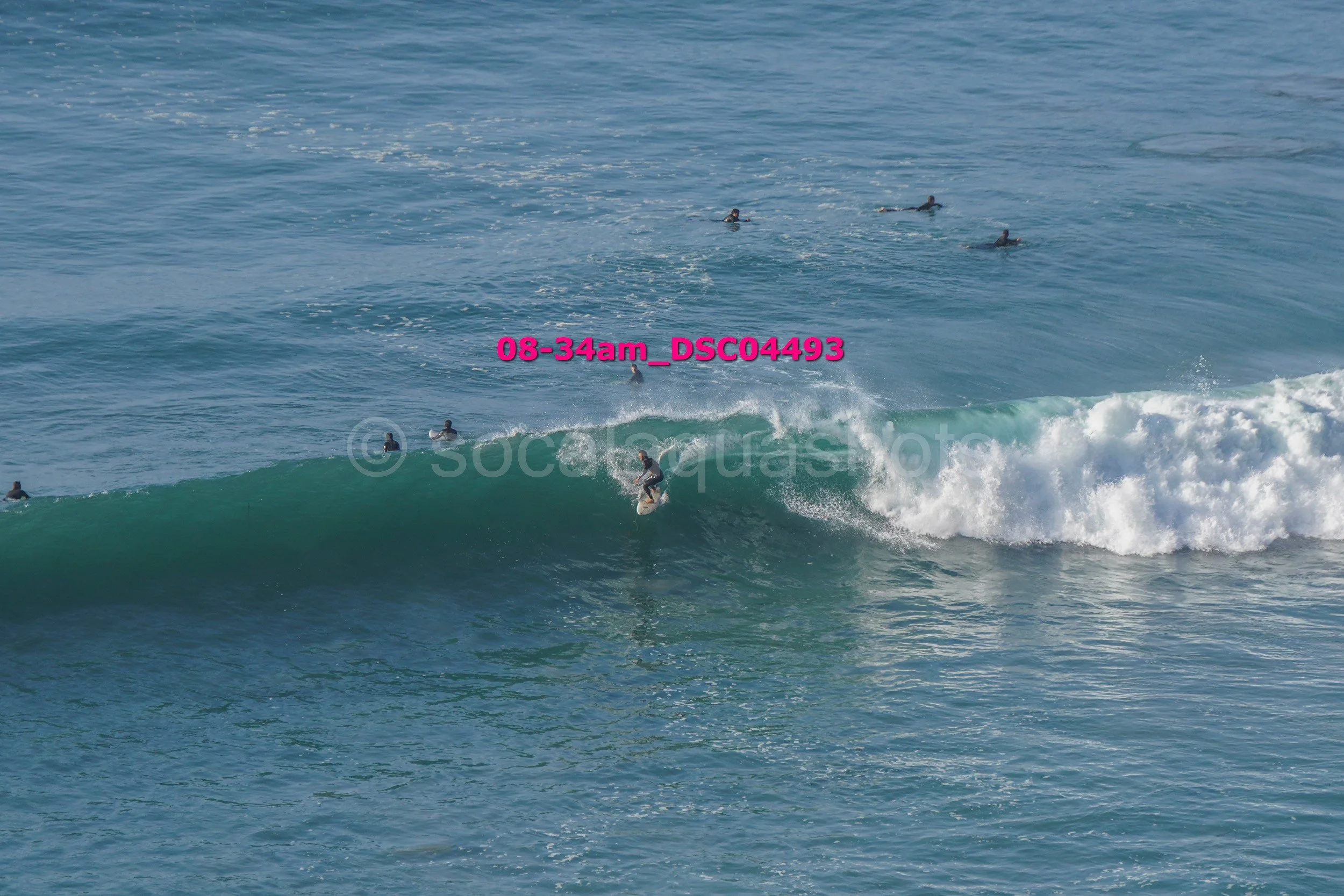 Surfer riding a wave in the ocean with several surfers in the background.