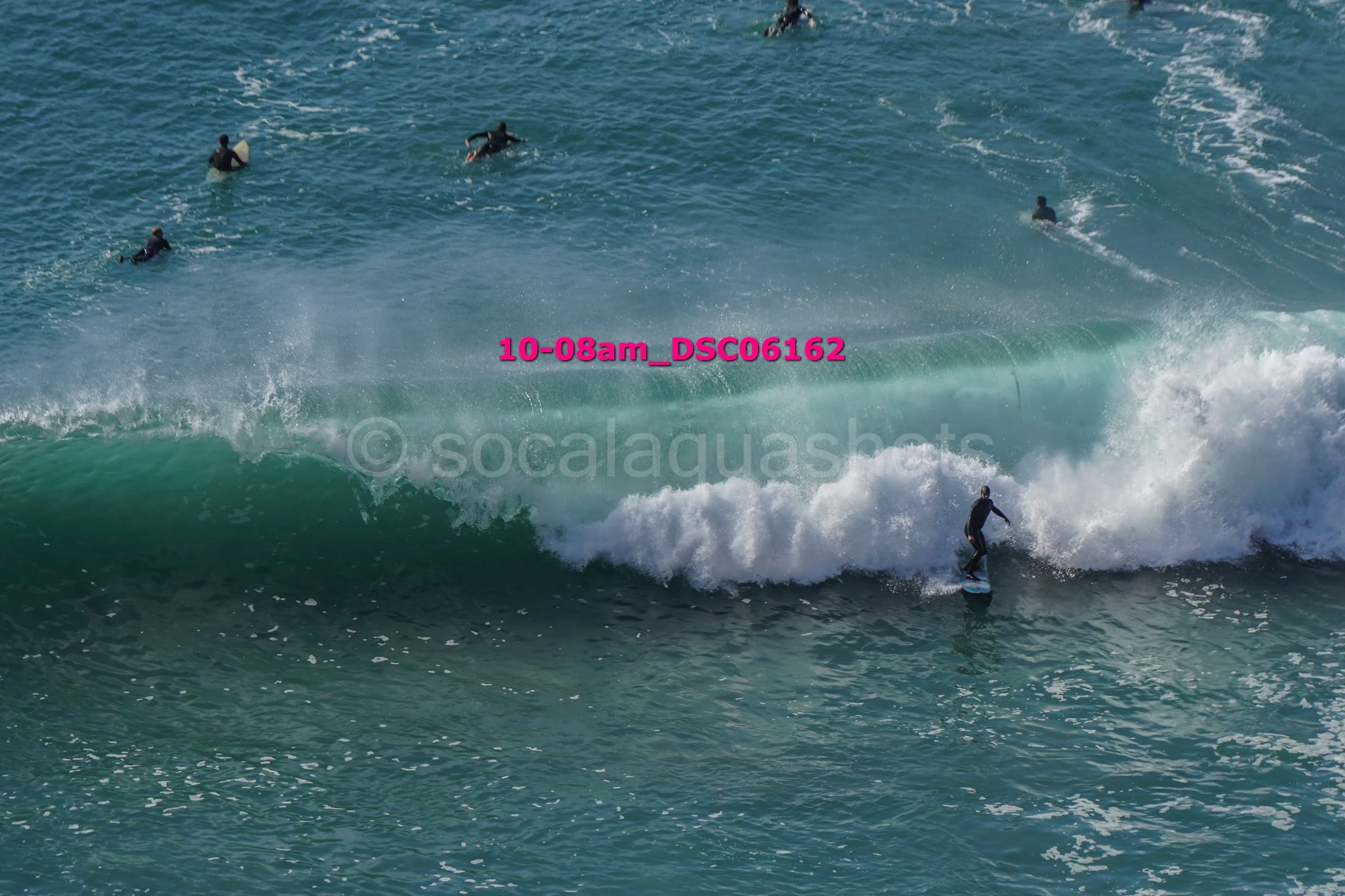 A person surfing a wave with several others swimming in the ocean nearby.