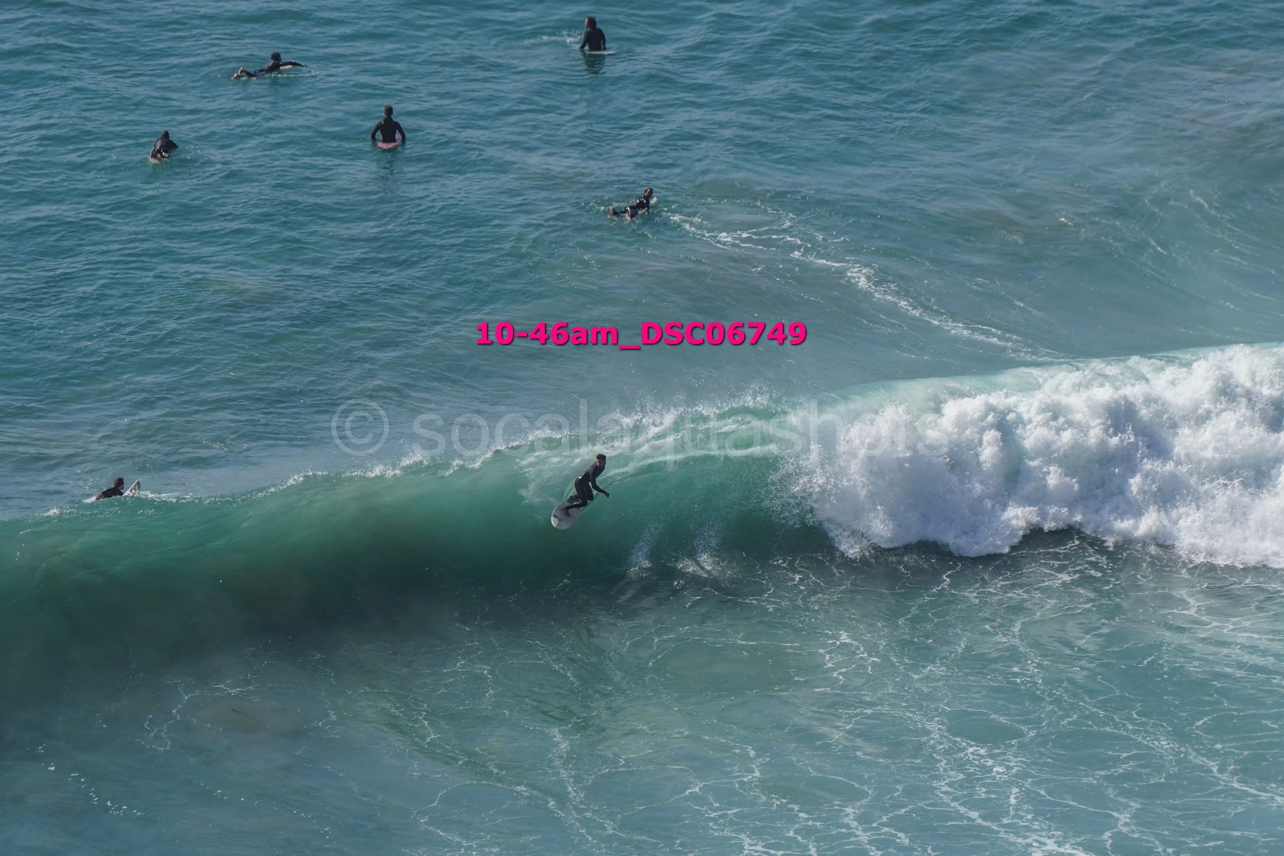 A person surfing a wave while several people swim in the ocean in the background.
