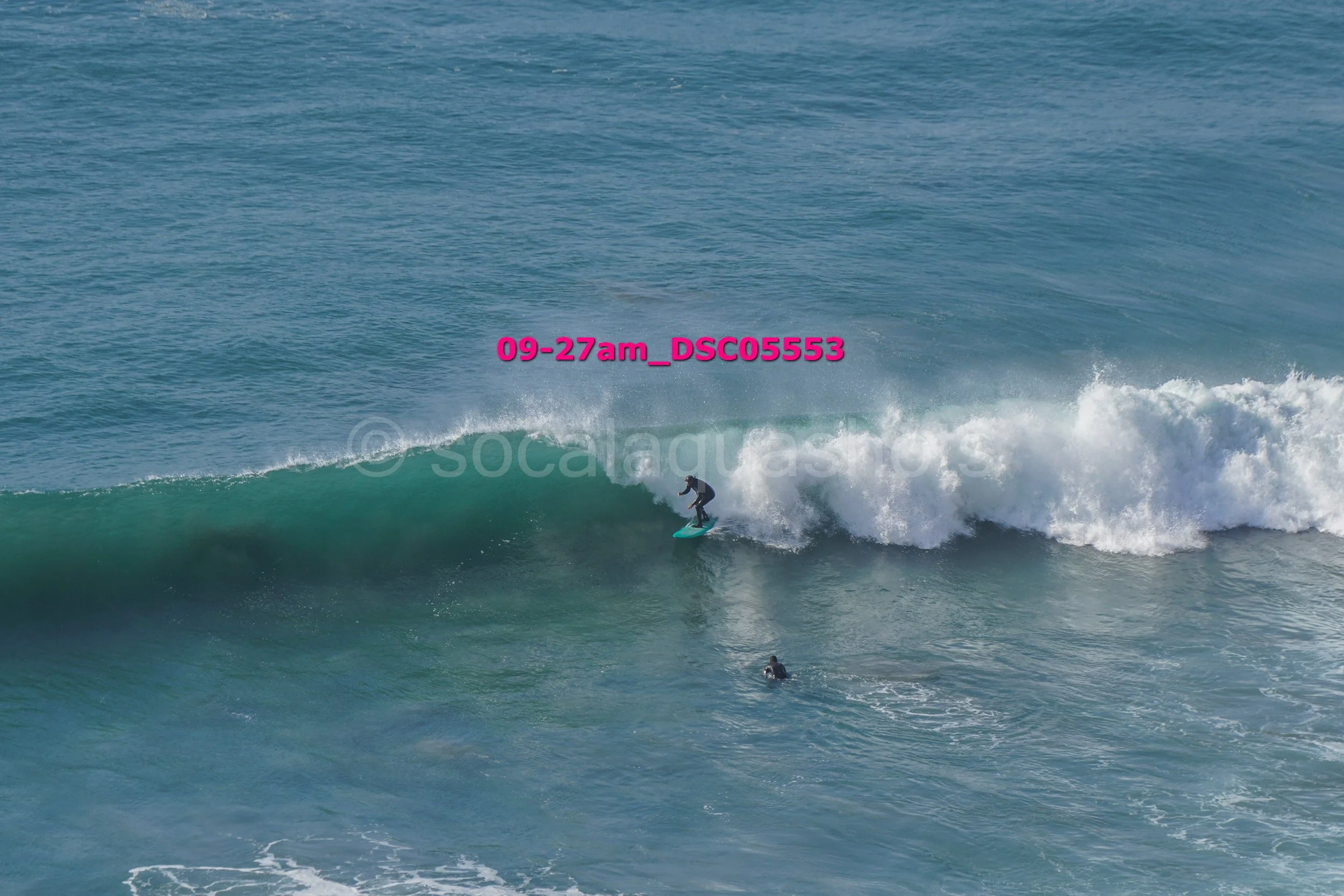 A person surfing on a wave in the ocean with another person swimming nearby.