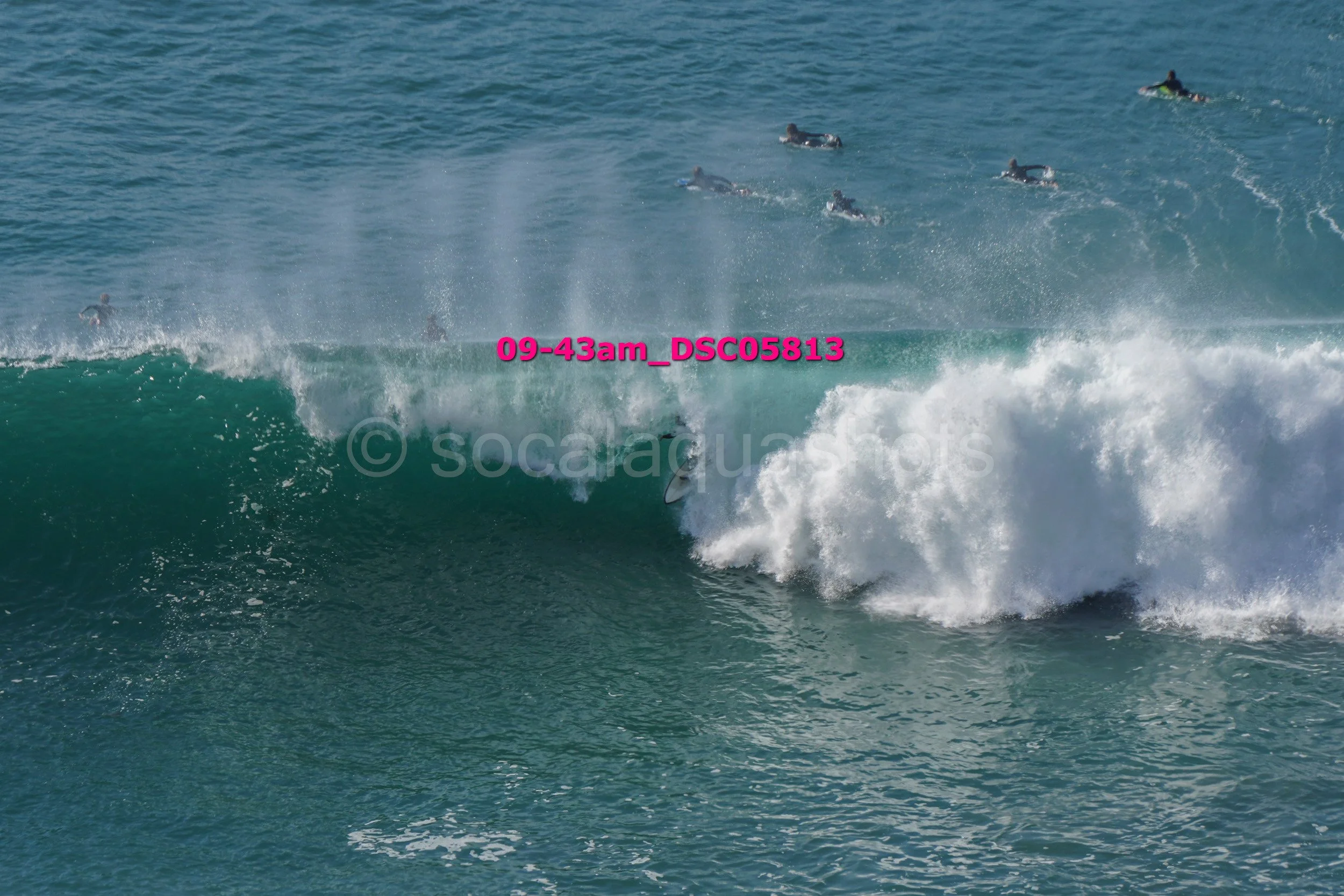A surfer riding a wave in the ocean with several people surfing in the background.
