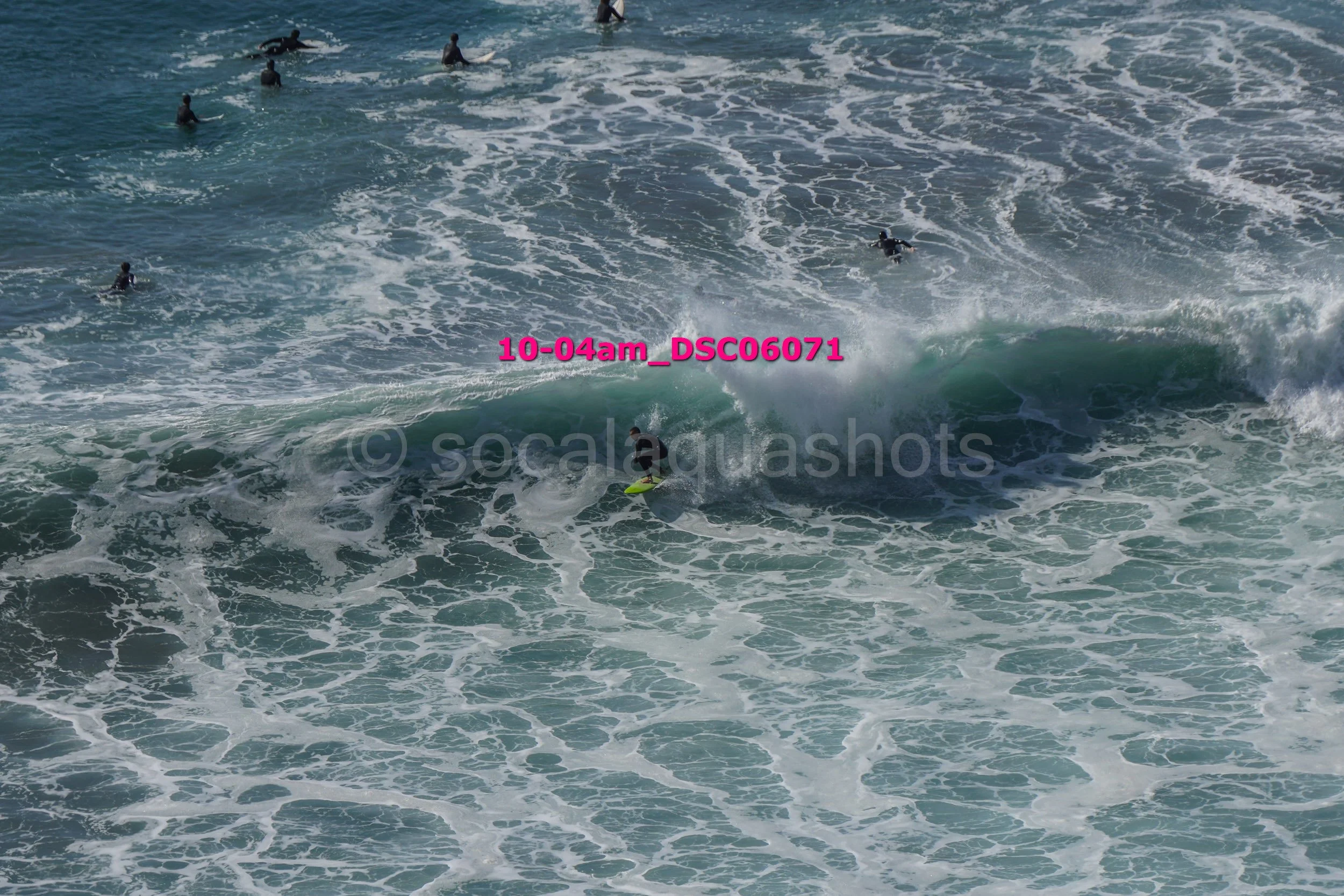 A group of surfers in the ocean, some riding a wave and others waiting in the water.