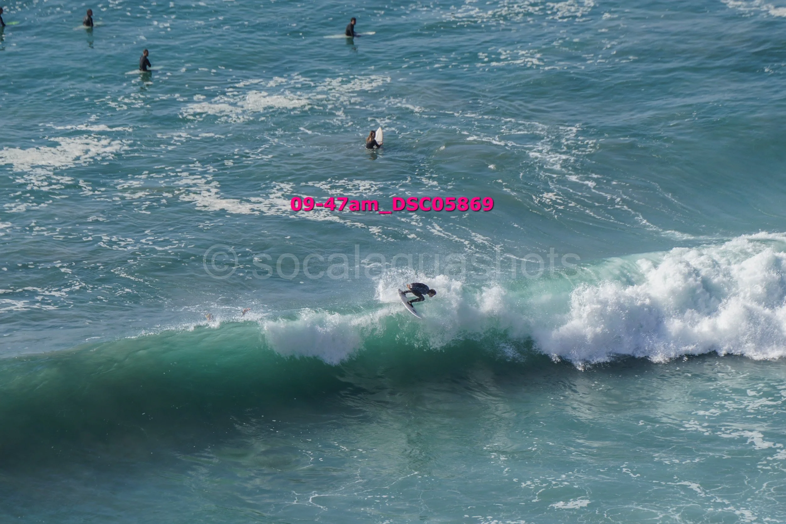 A person surfing on a wave in the ocean with others in the water in the background.
