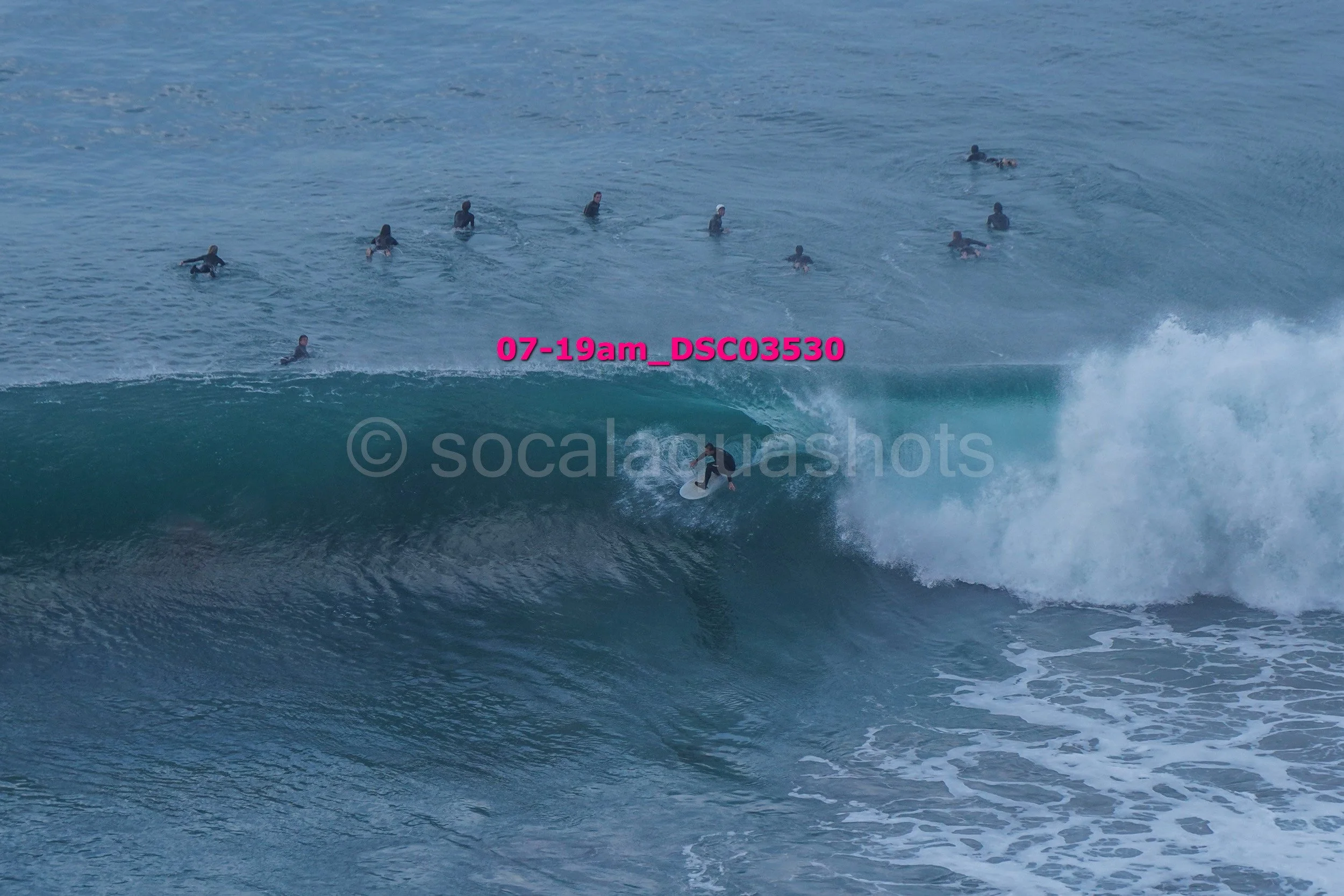 Surfer riding a large wave while a group of surfers in the background watch from the ocean
