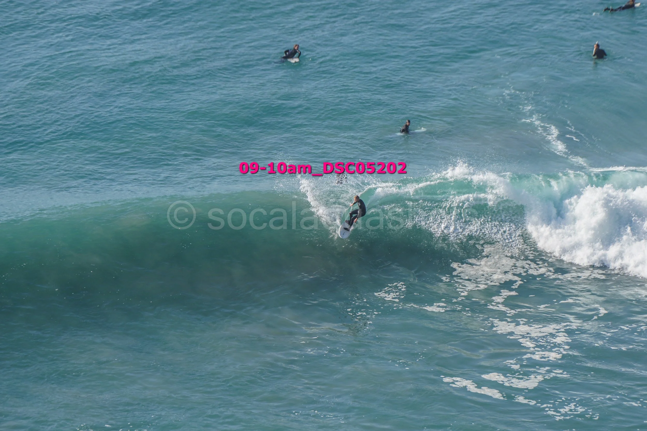 Surfer riding a wave with several people in the water in the background.