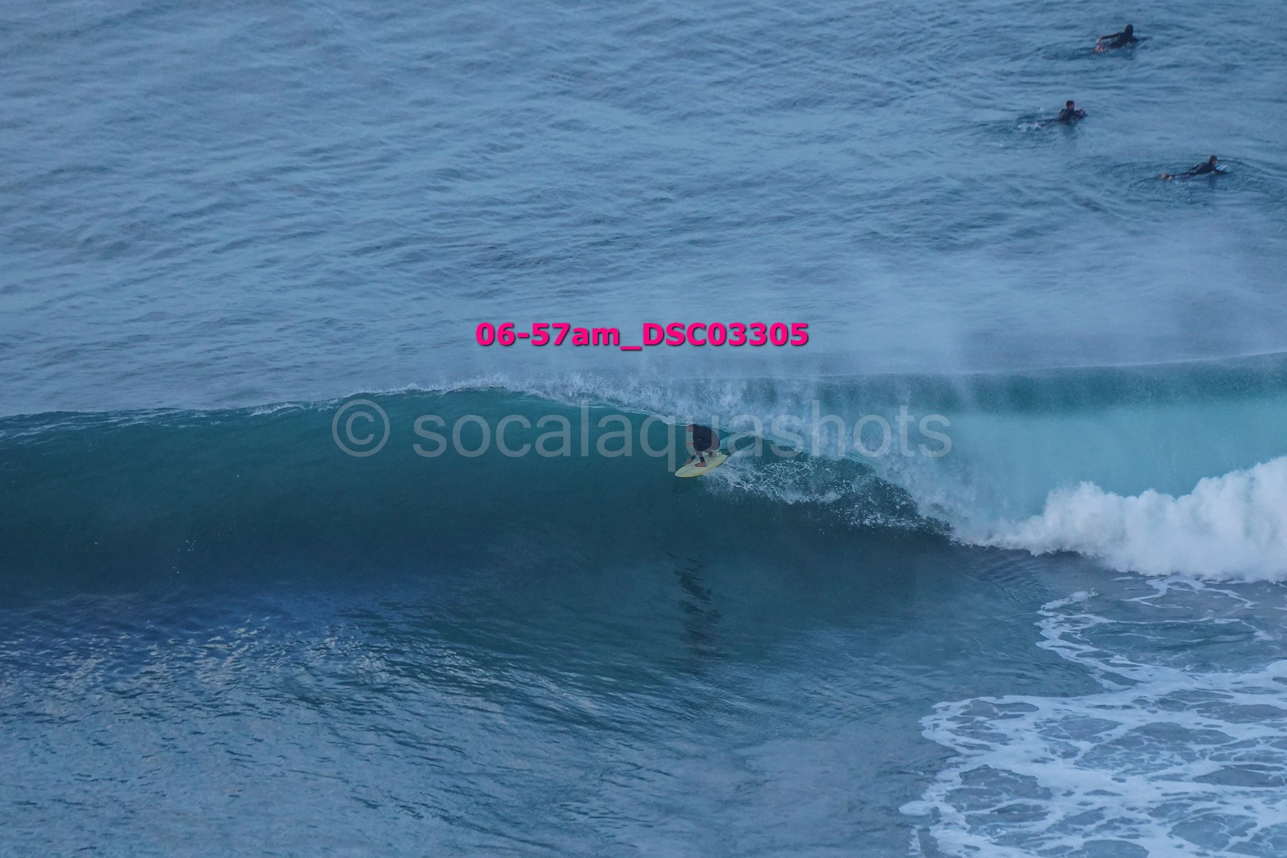 A person surfing on a wave in the ocean with other surfers in the distance.